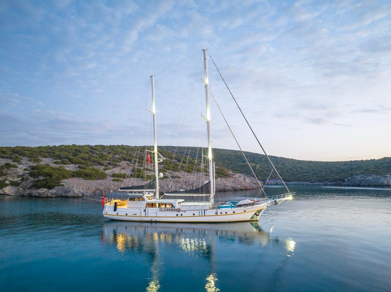 White traditional gulet with two masts anchored in turquoise Mediterranean bay at sunset