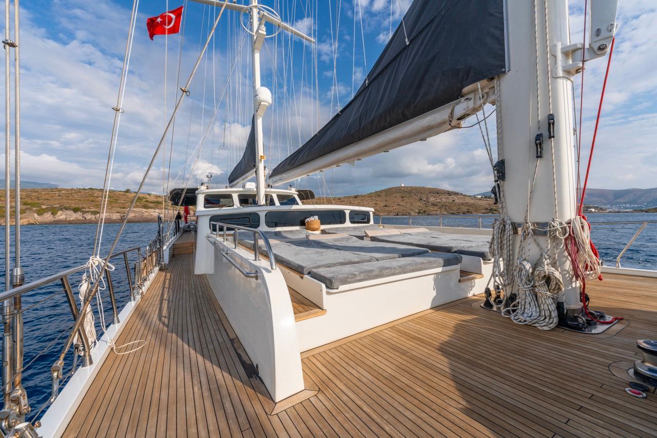 Gulet bow deck with white cushioned sunbeds, sailing rigging, and teak decking