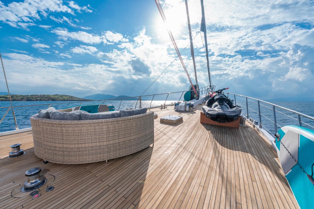 yacht deck with stored jet ski and curved wicker seating area under rigging