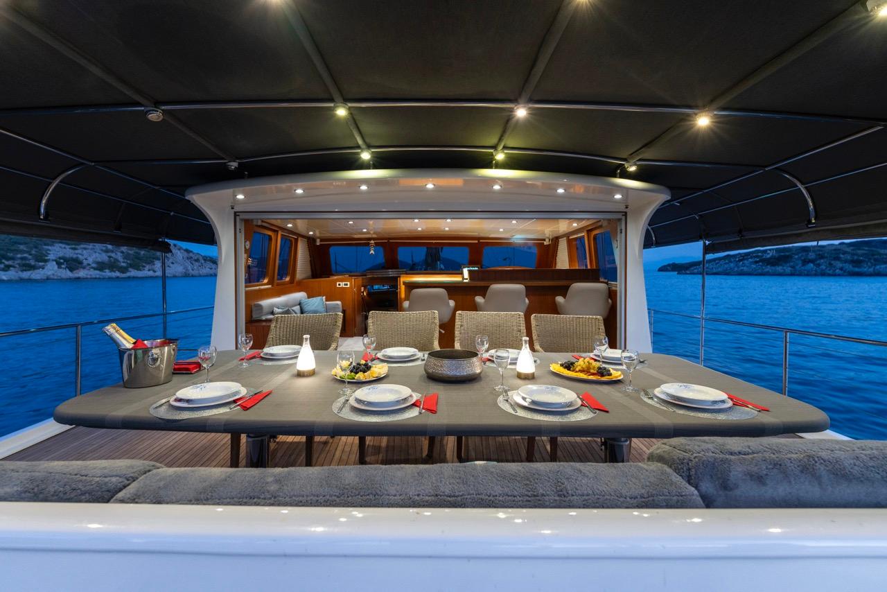 yacht aft deck dining area with table set for eight guests, plated food and wine bottles