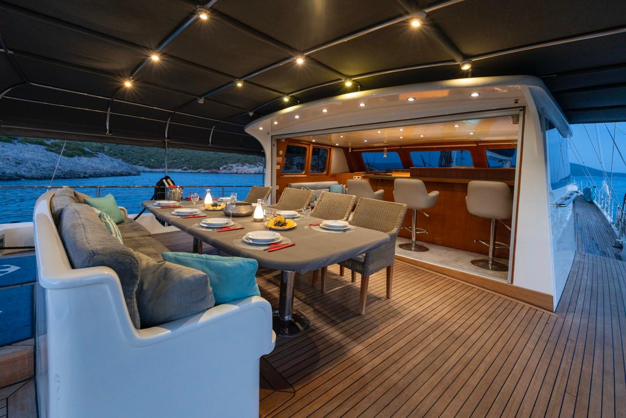 yacht aft deck with outdoor dining table and white cushioned seating under black awning