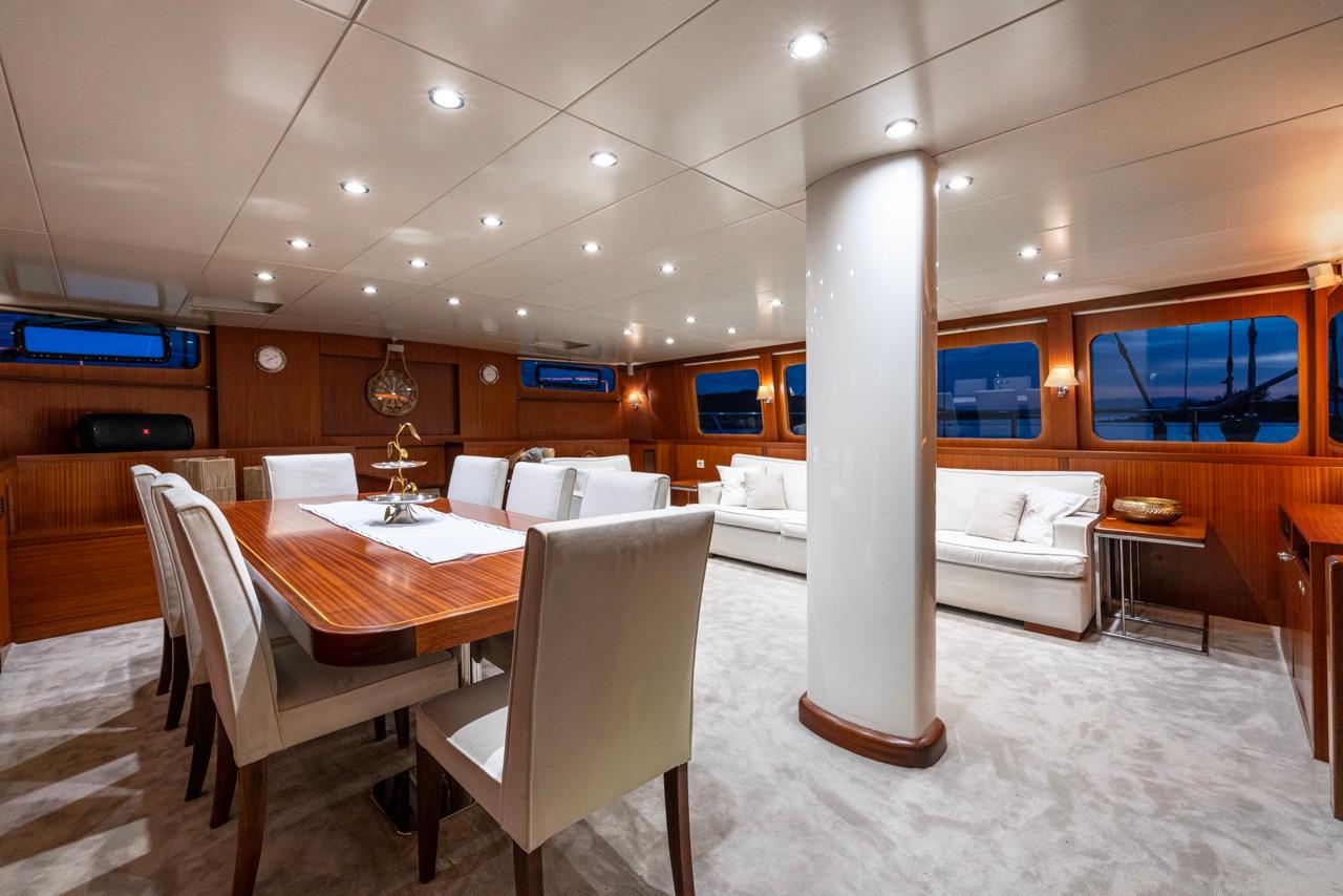 yacht interior salon with wooden dining table, white chairs and built-in seating area