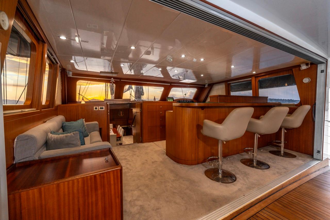 yacht main salon with grey sofa, white bar stools, and teak woodwork