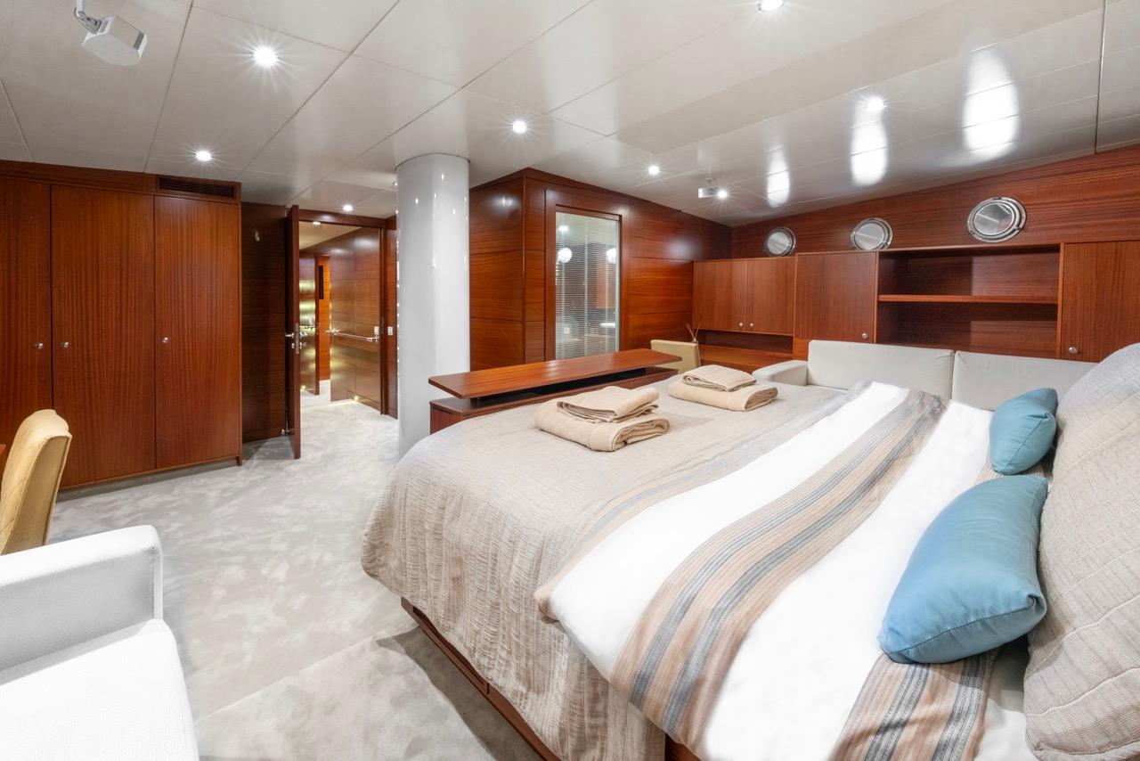luxury yacht cabin featuring double bed with striped linens, rich wood paneling, and built-in wardrobes