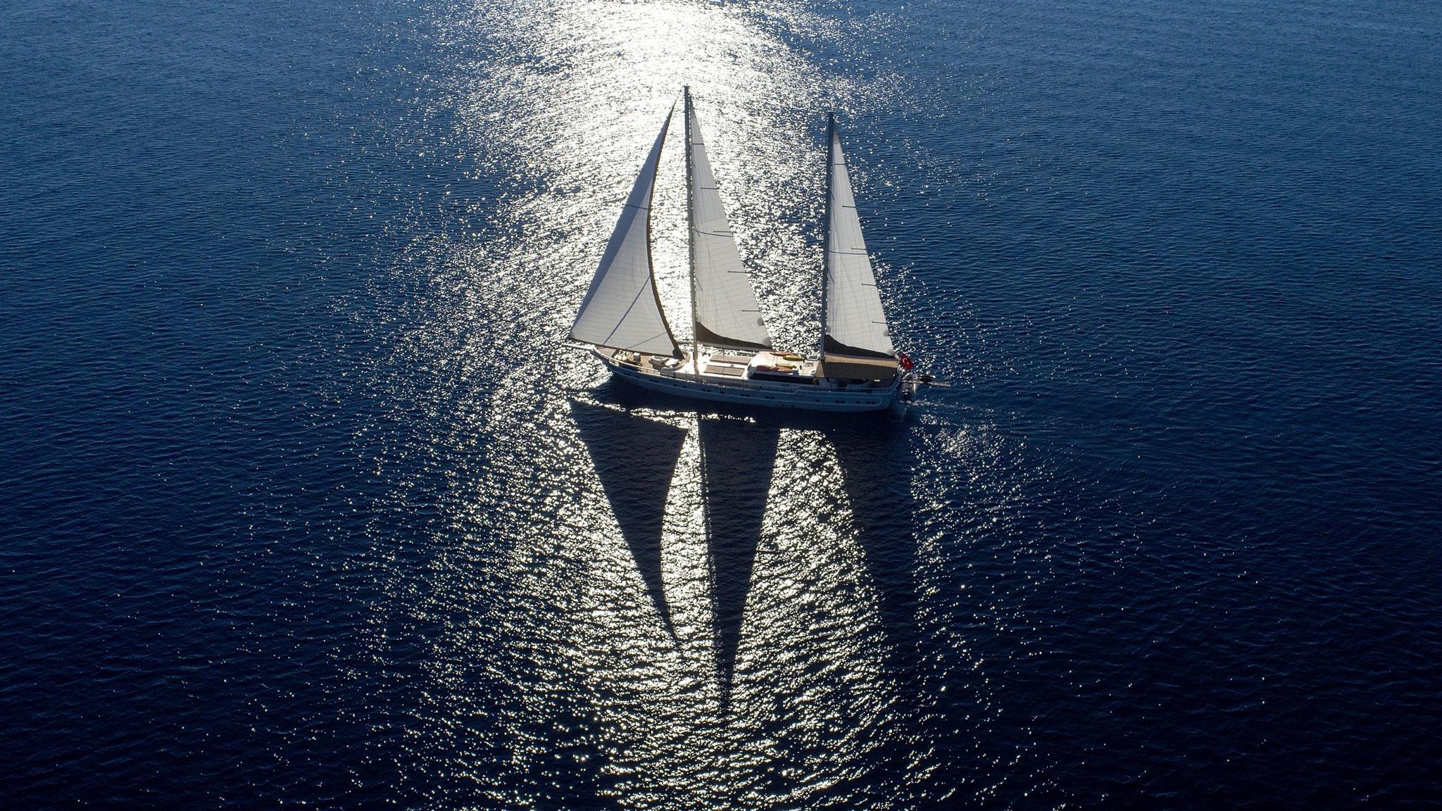 aerial view of traditional sailing yacht with white sails deployed on deep blue Mediterranean waters