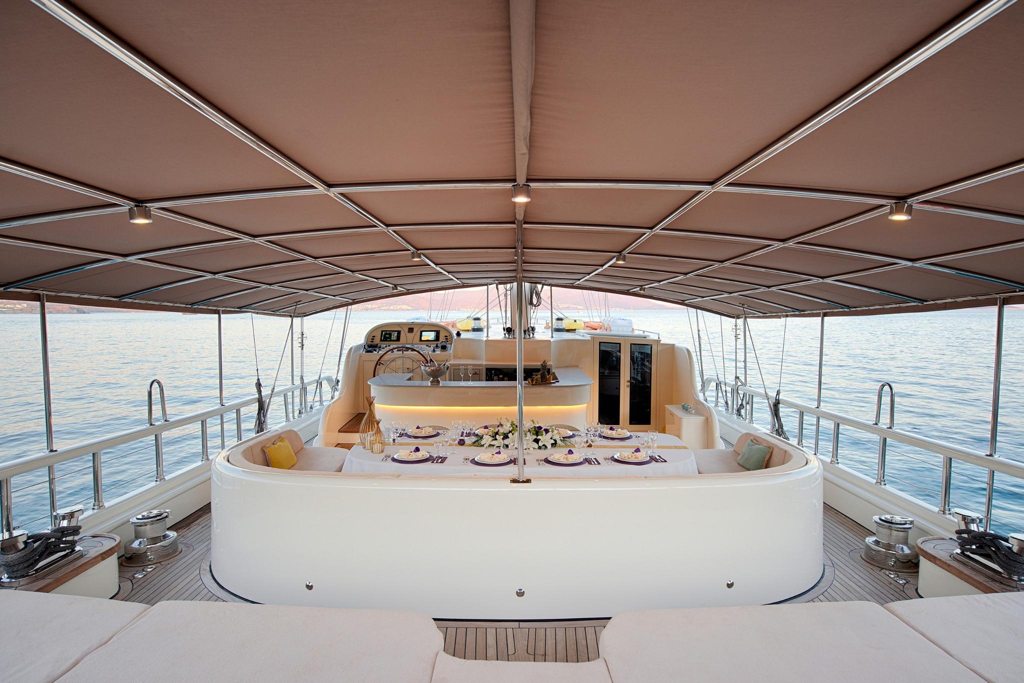 yacht aft deck with curved seating area, formal dining table setting and helm station