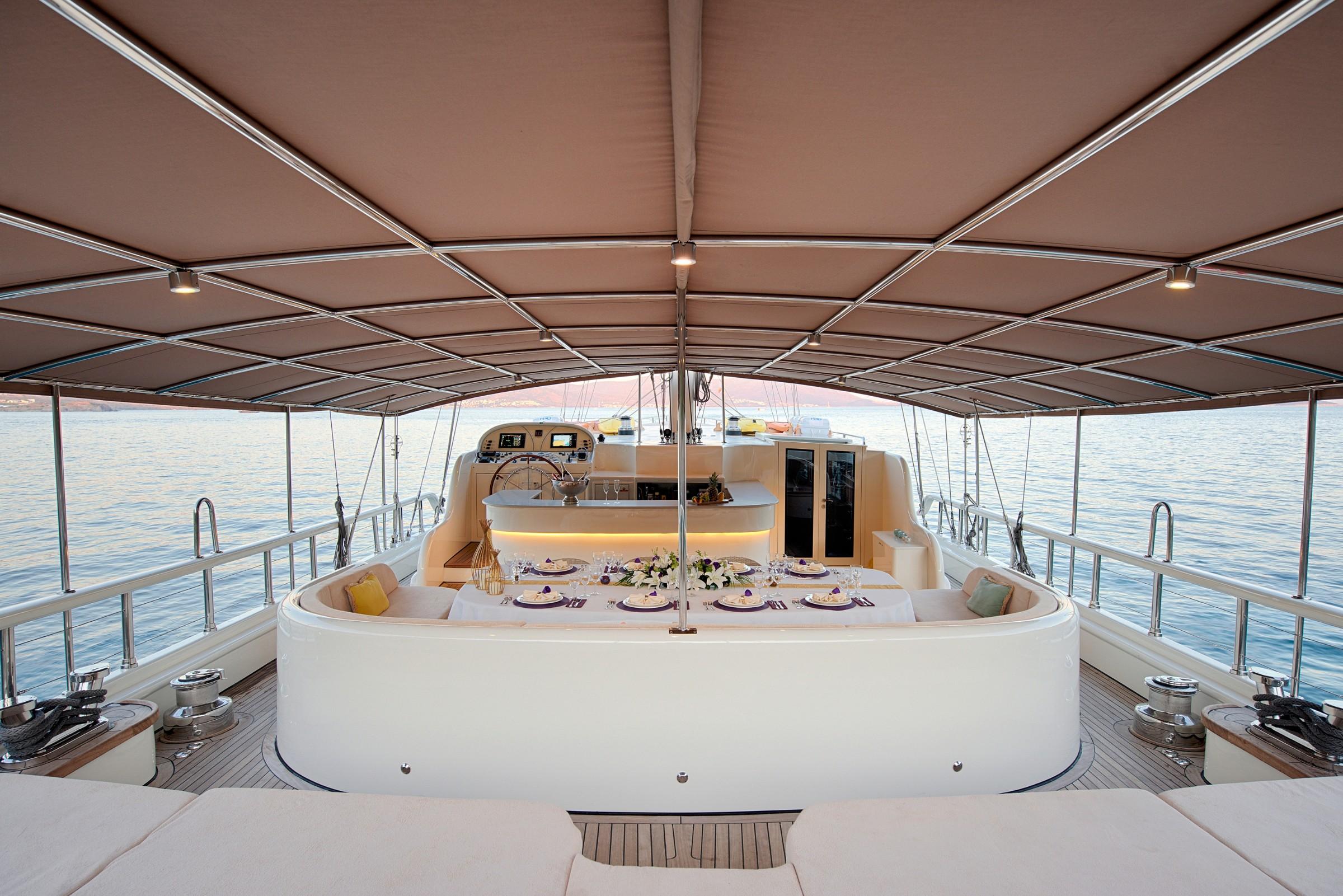 yacht aft deck with curved seating area, formal dining table setting and helm station
