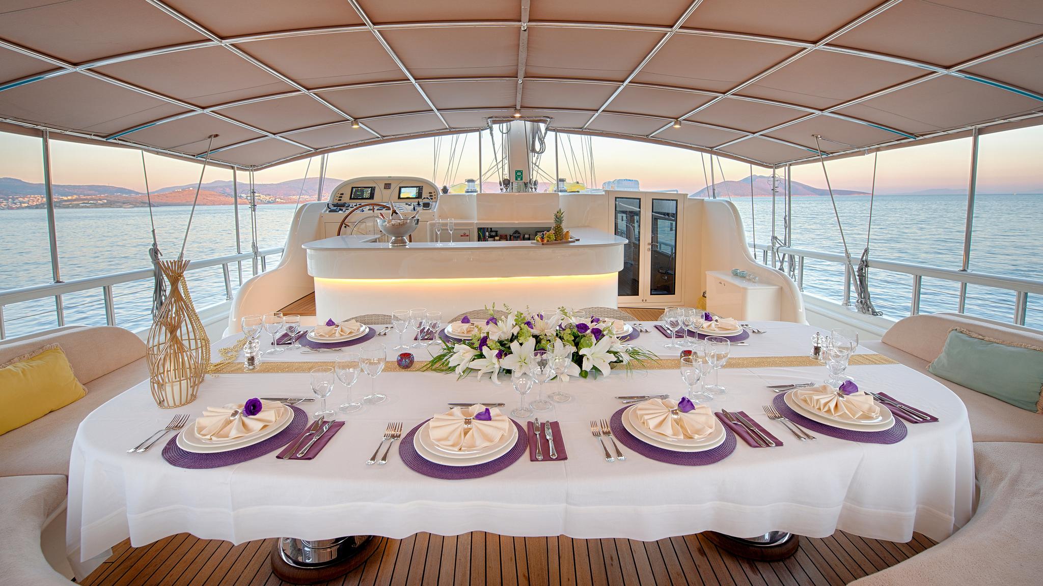 elegant dining table formally set with purple placemats, white linens, and floral centerpiece on yacht deck