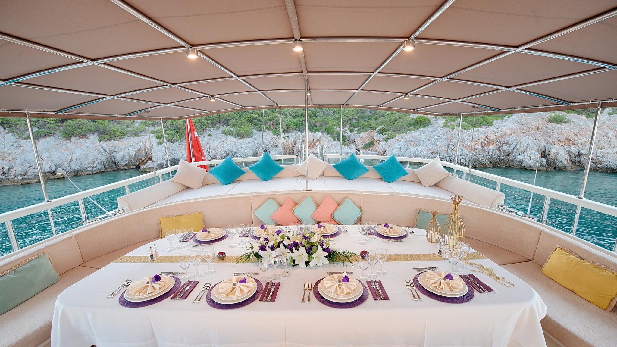 aft deck dining area with formal table setting and cushioned seating overlooking rocky coastline