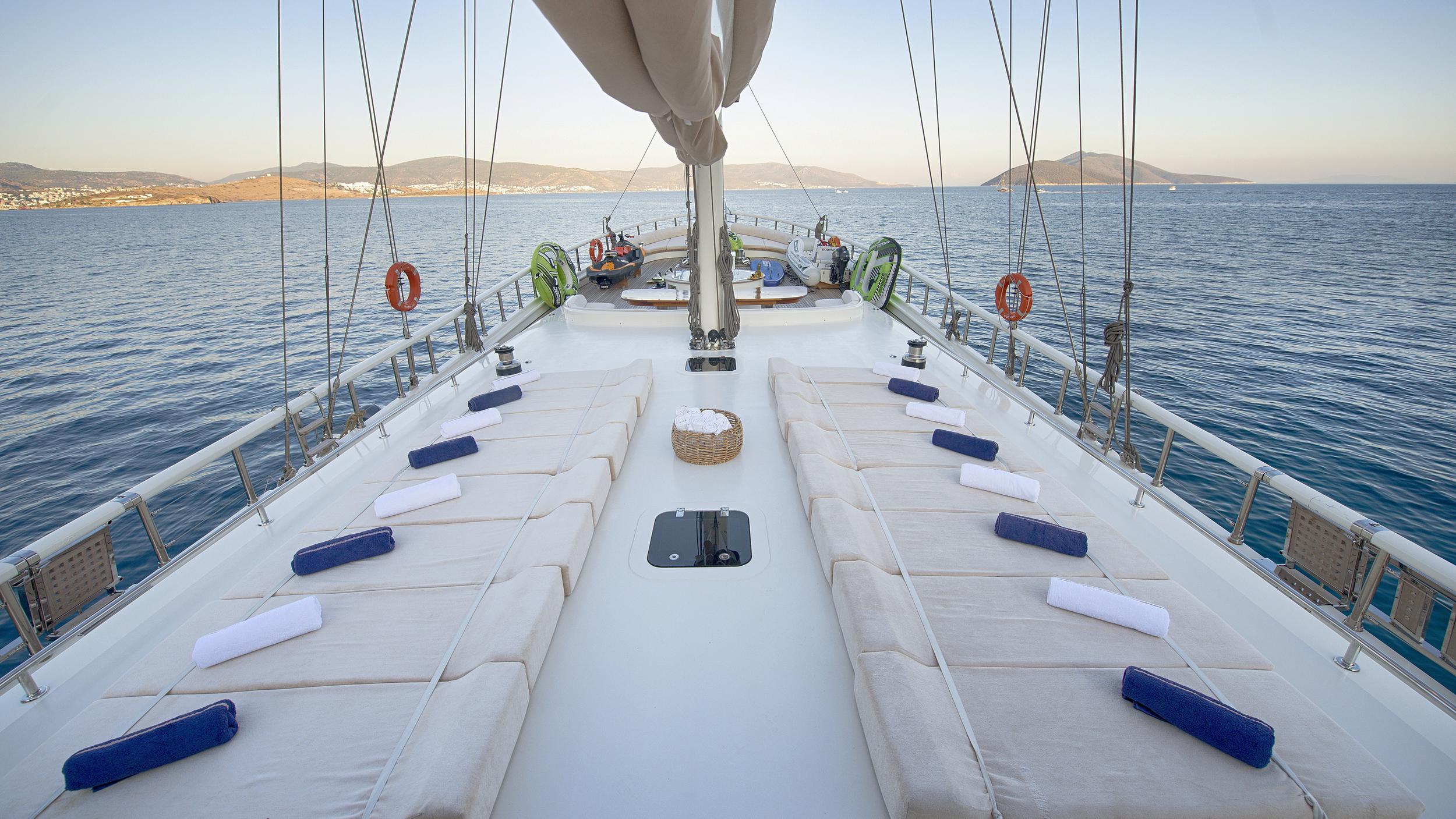 bow deck with white cushioned lounging pads, navy blue pillows and mast rigging