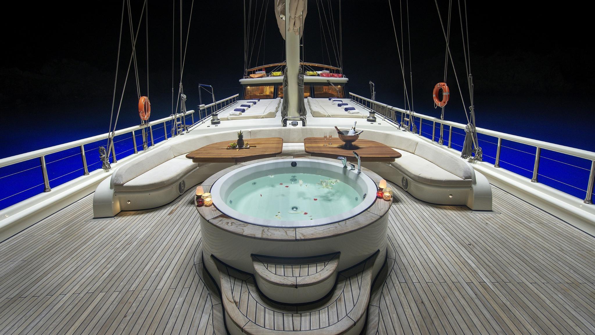 yacht foredeck jacuzzi with curved white seating and teak tables at night