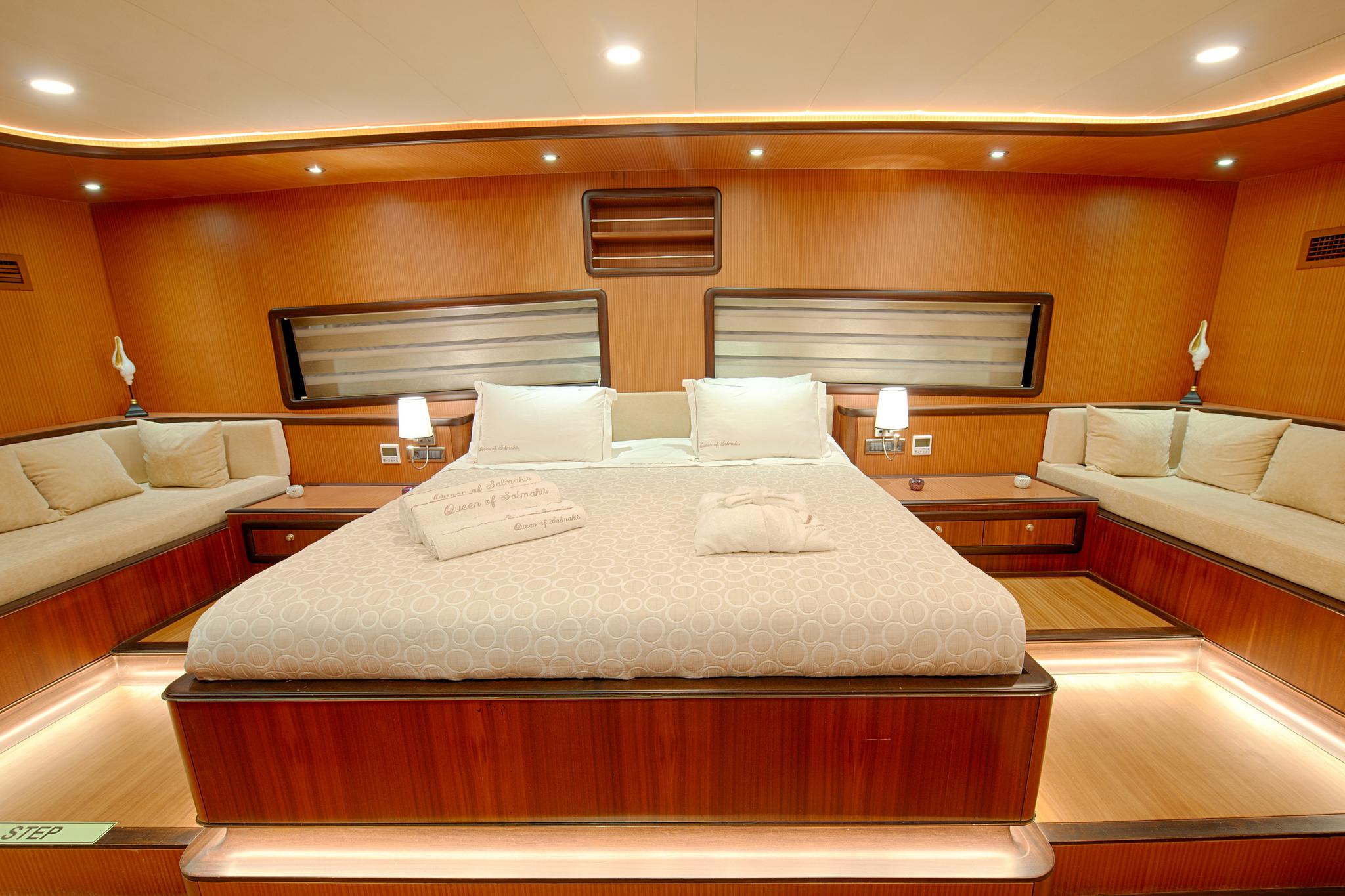 luxury yacht master cabin featuring king bed with cream bedding and rich wood paneling