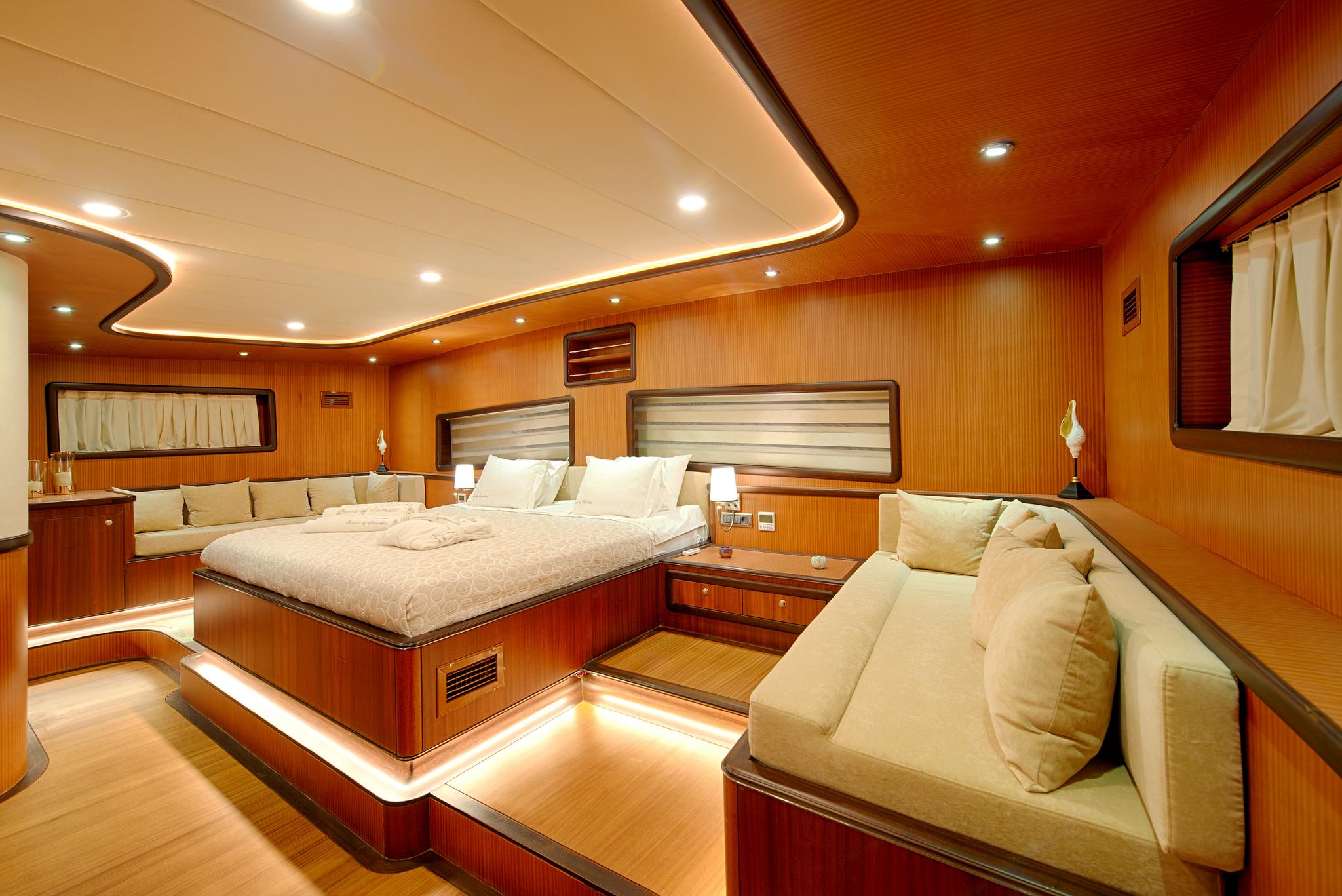 master cabin interior featuring king bed, cream seating area, wood paneling and recessed lighting