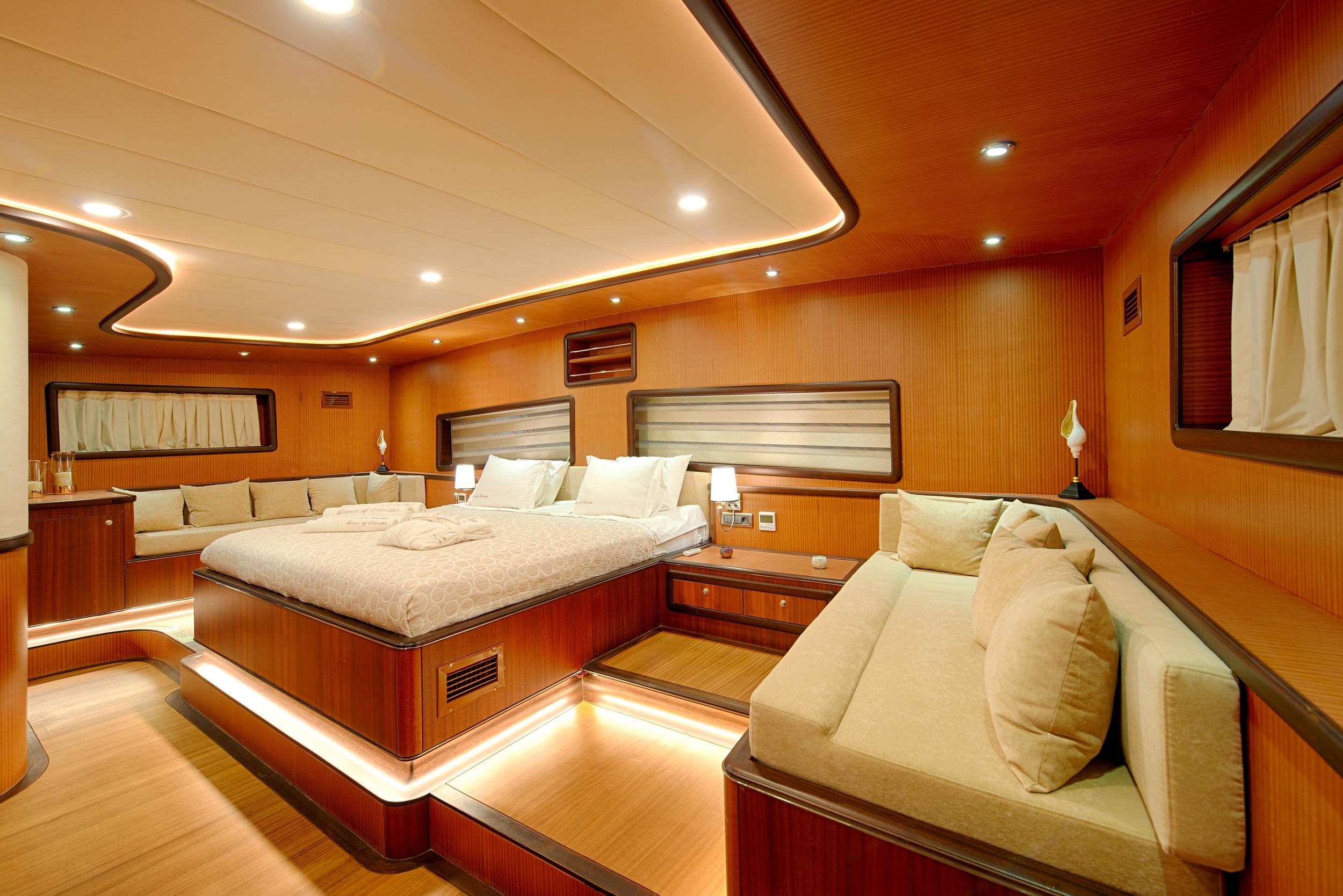 master cabin interior featuring king bed, cream seating area, wood paneling and recessed lighting
