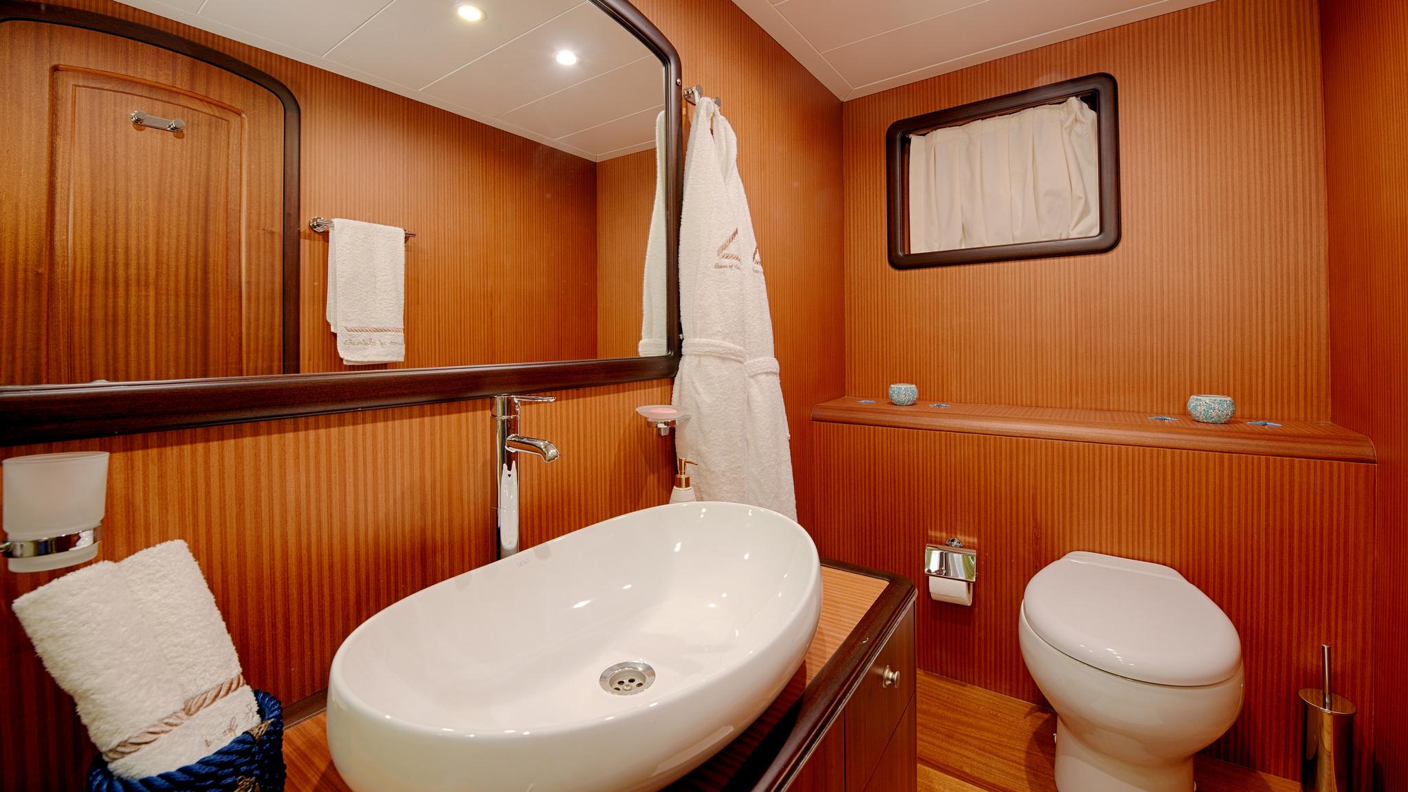 yacht ensuite bathroom with white oval basin, toilet and warm wood paneling