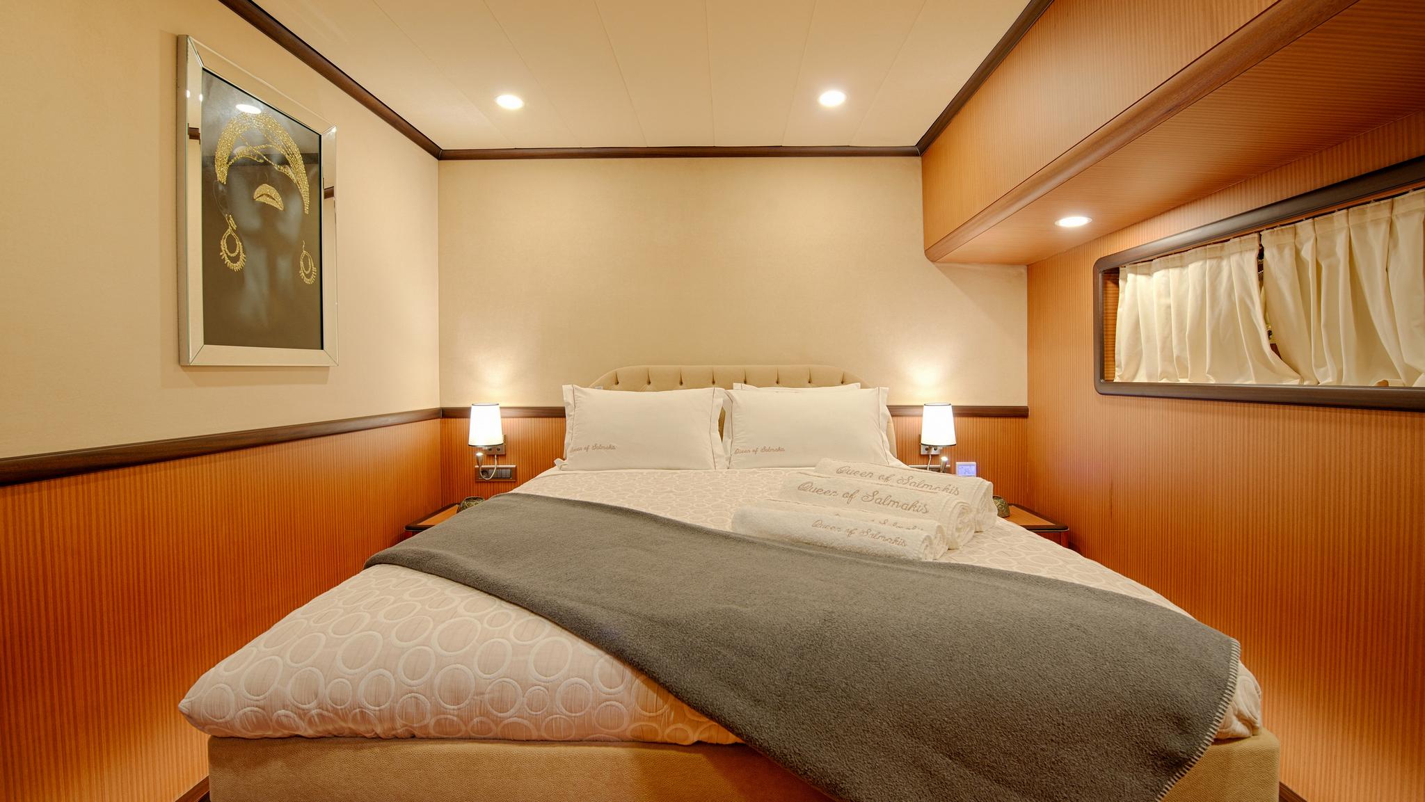 yacht cabin with double bed, cream upholstered headboard, wood paneling and bedside reading lights
