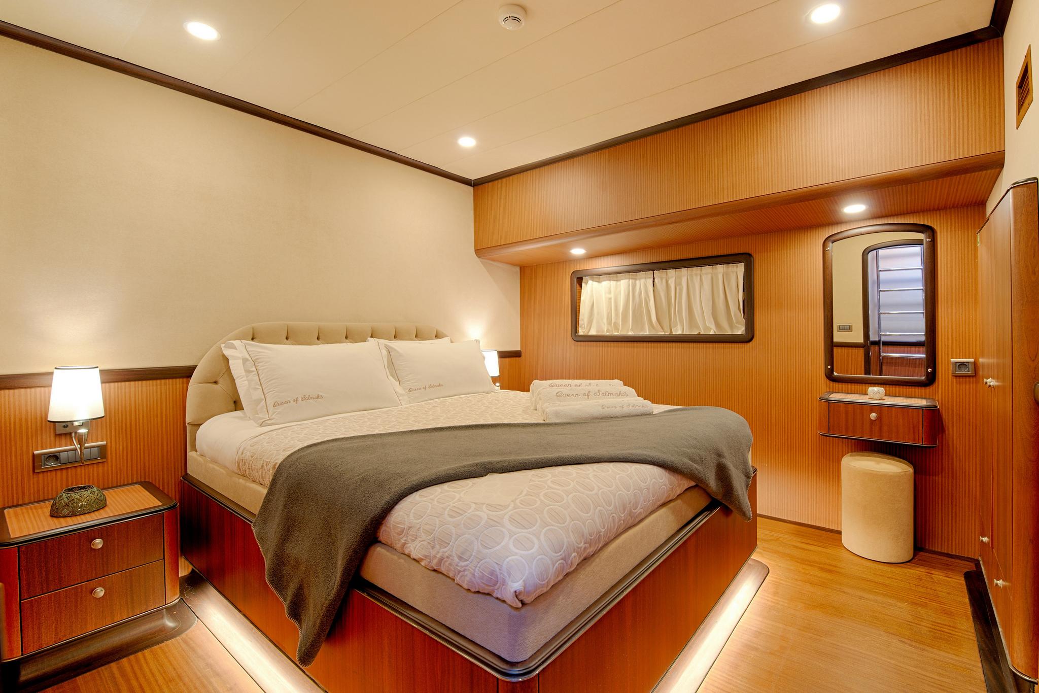 Master cabin interior featuring king bed with tufted headboard, rich wood paneling, bedside tables and vanity area