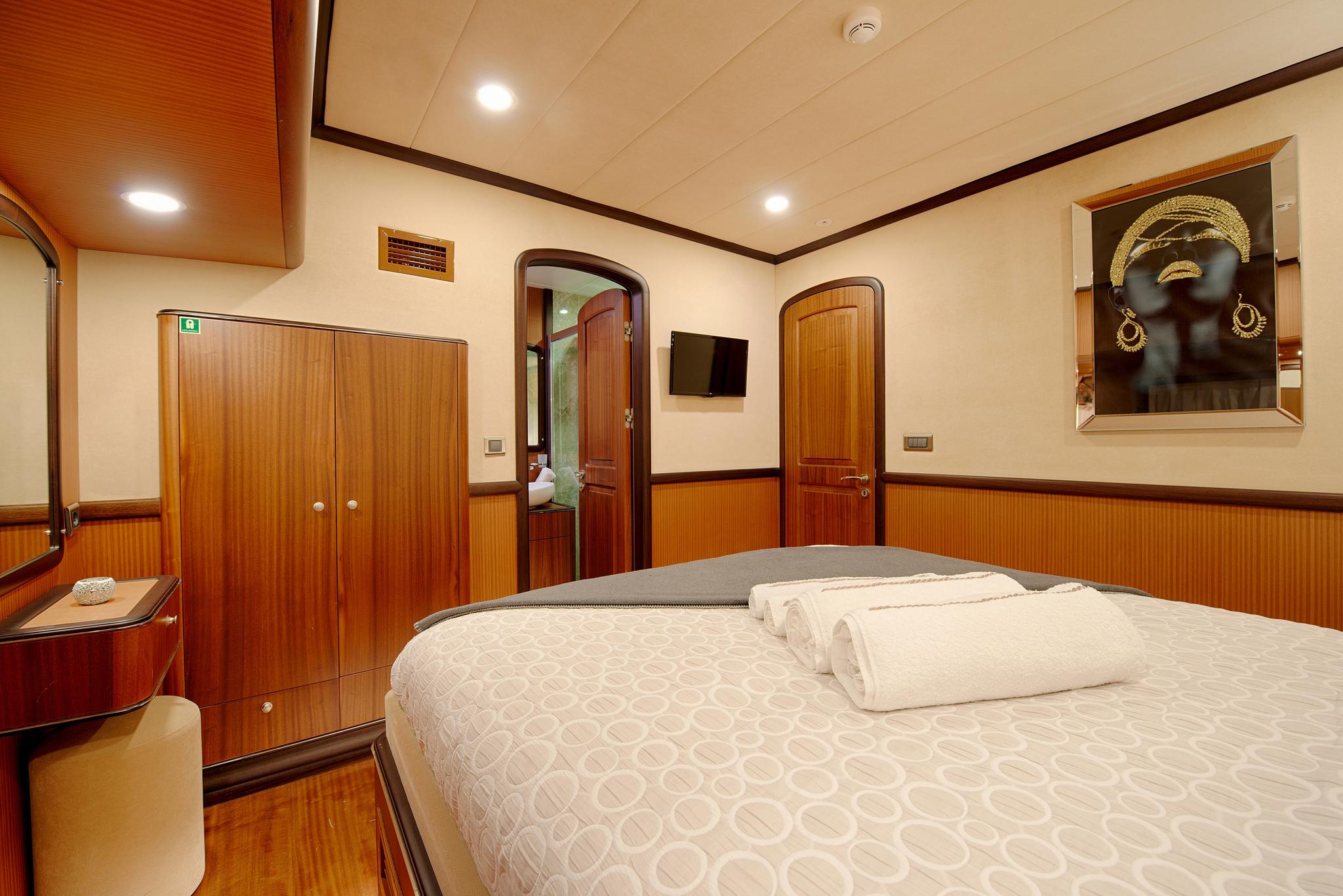 yacht cabin interior with double bed, wooden paneling, built-in wardrobes and en-suite entrance