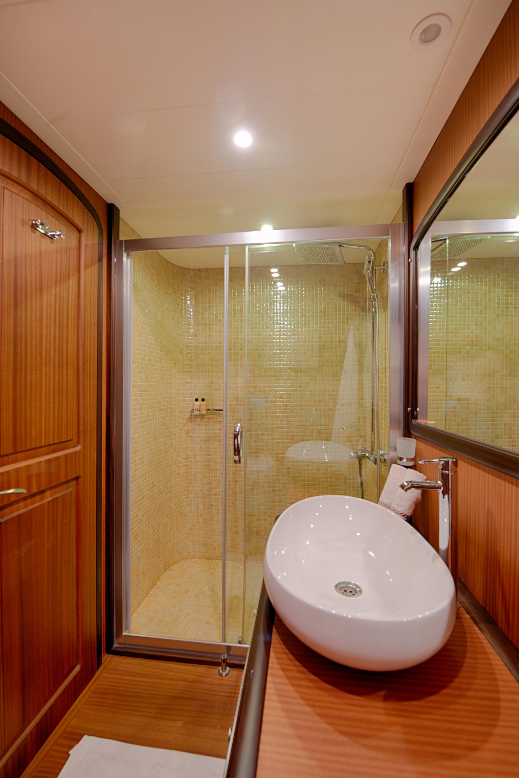 yacht bathroom featuring glass shower enclosure, white vessel sink on wooden counter, and golden mosaic tiles