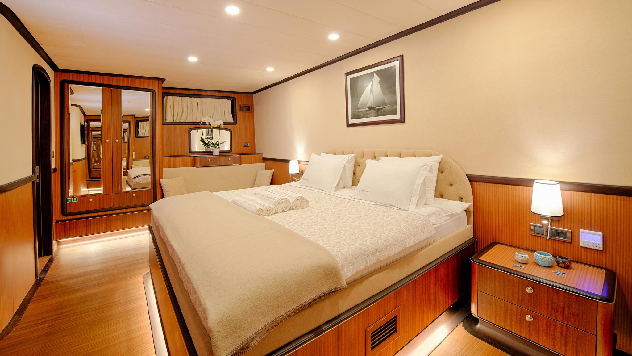 yacht cabin interior with white bedding, wooden paneling, nautical artwork and built-in furniture