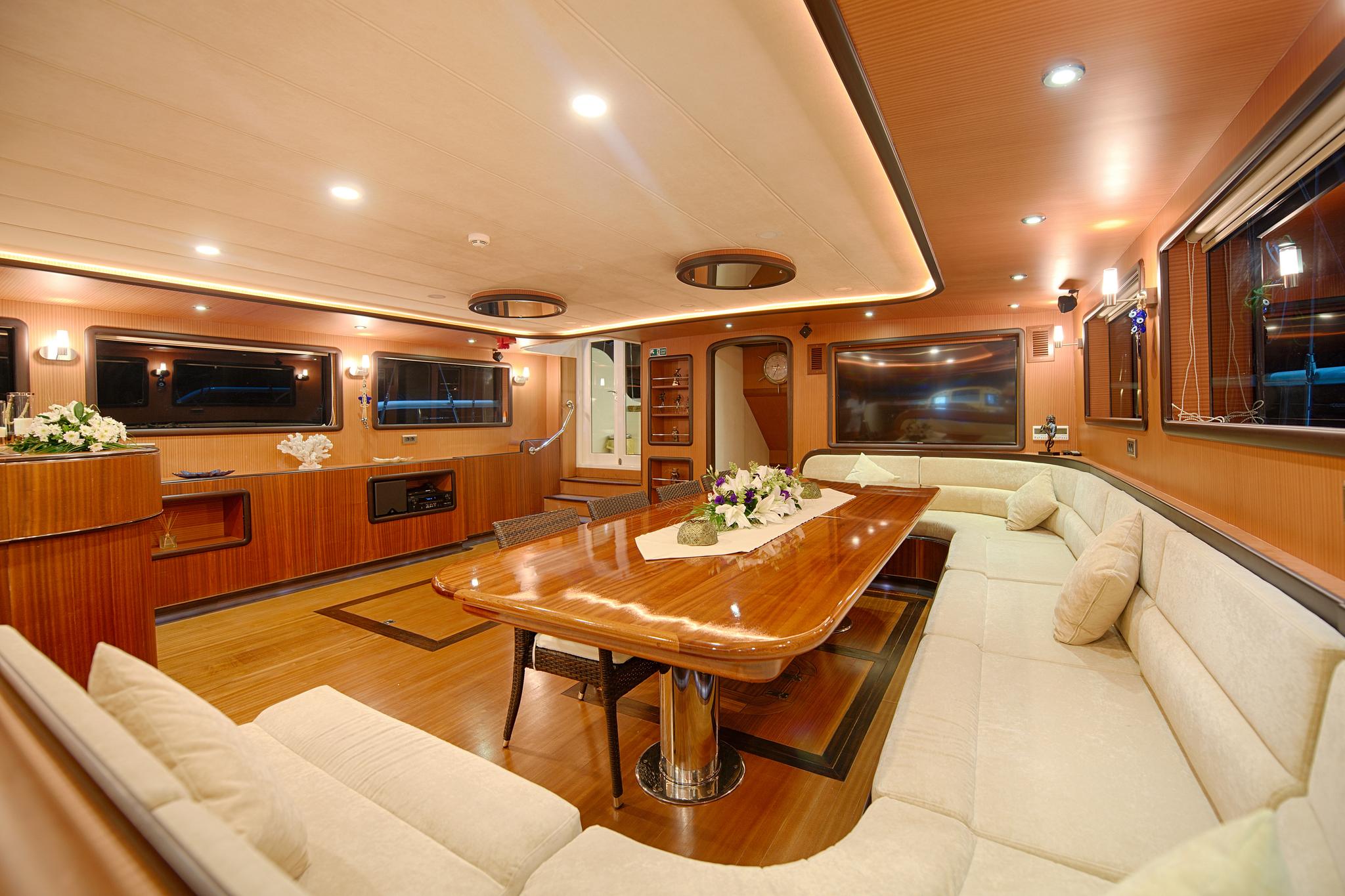 yacht main salon with polished wood dining table, cream leather seating and entertainment system