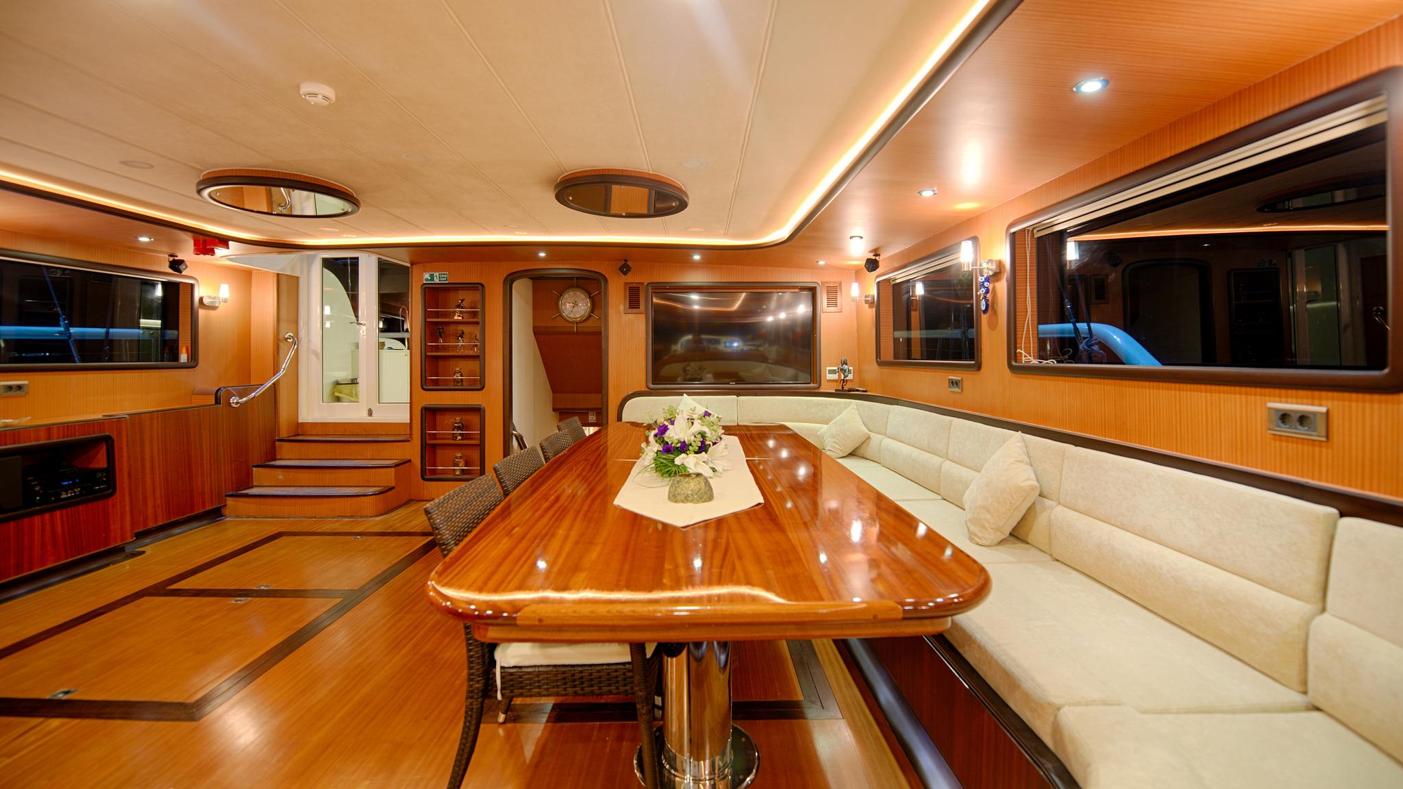 luxury yacht main salon with polished wood dining table, cream upholstered seating, and entertainment system