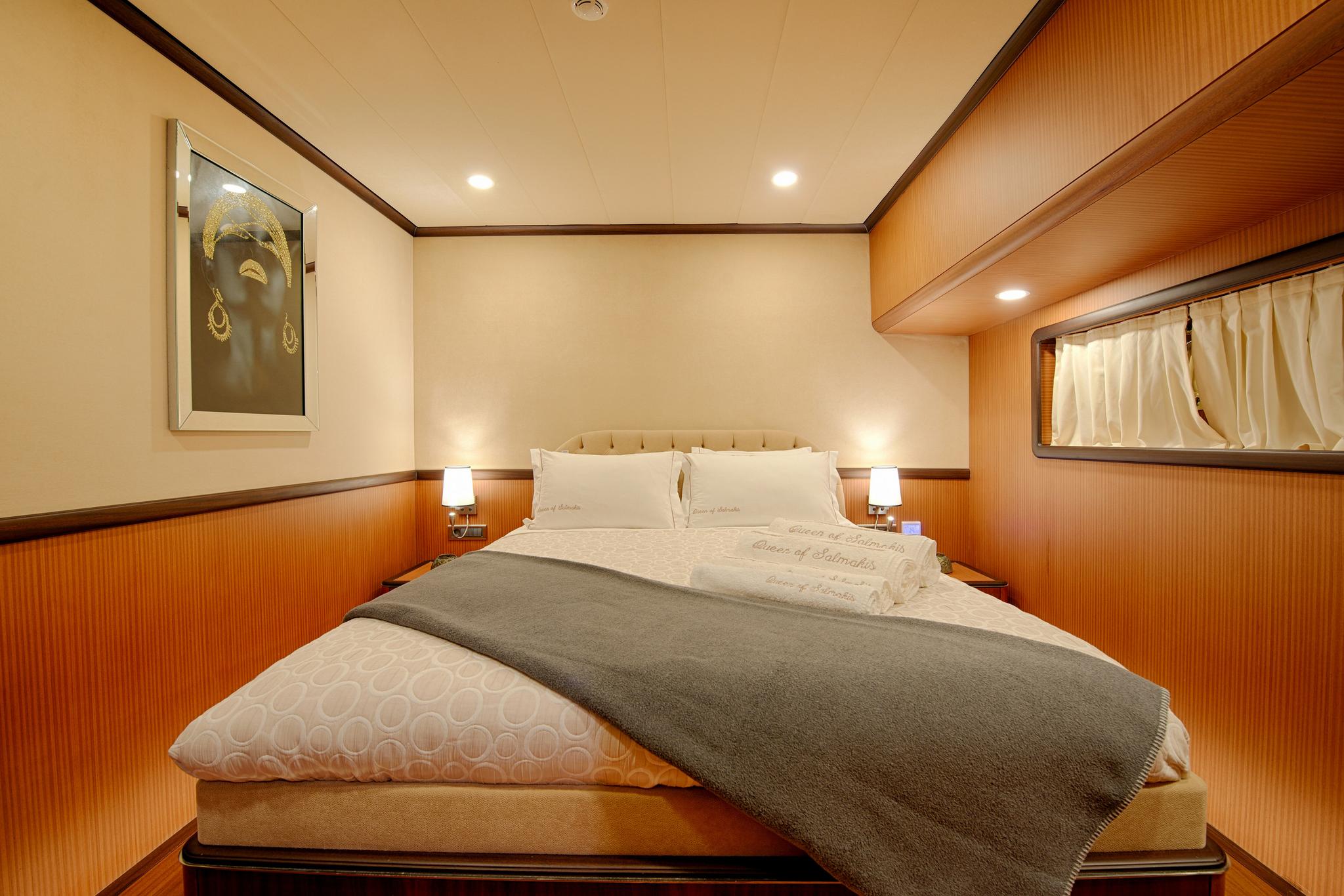 yacht cabin with double bed, wooden paneling, bedside lamps and porthole window