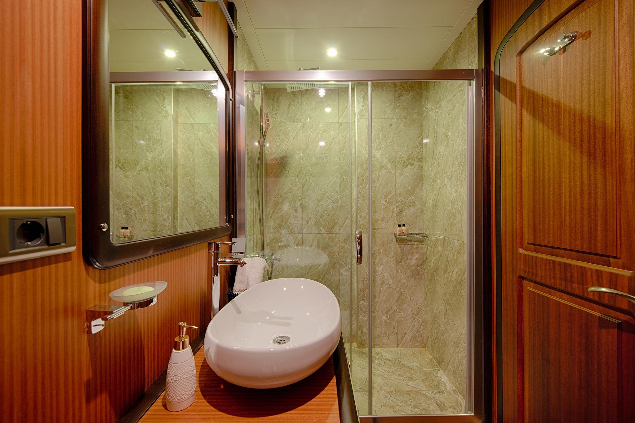 luxury yacht bathroom featuring white oval vessel sink, glass enclosed shower with marble walls