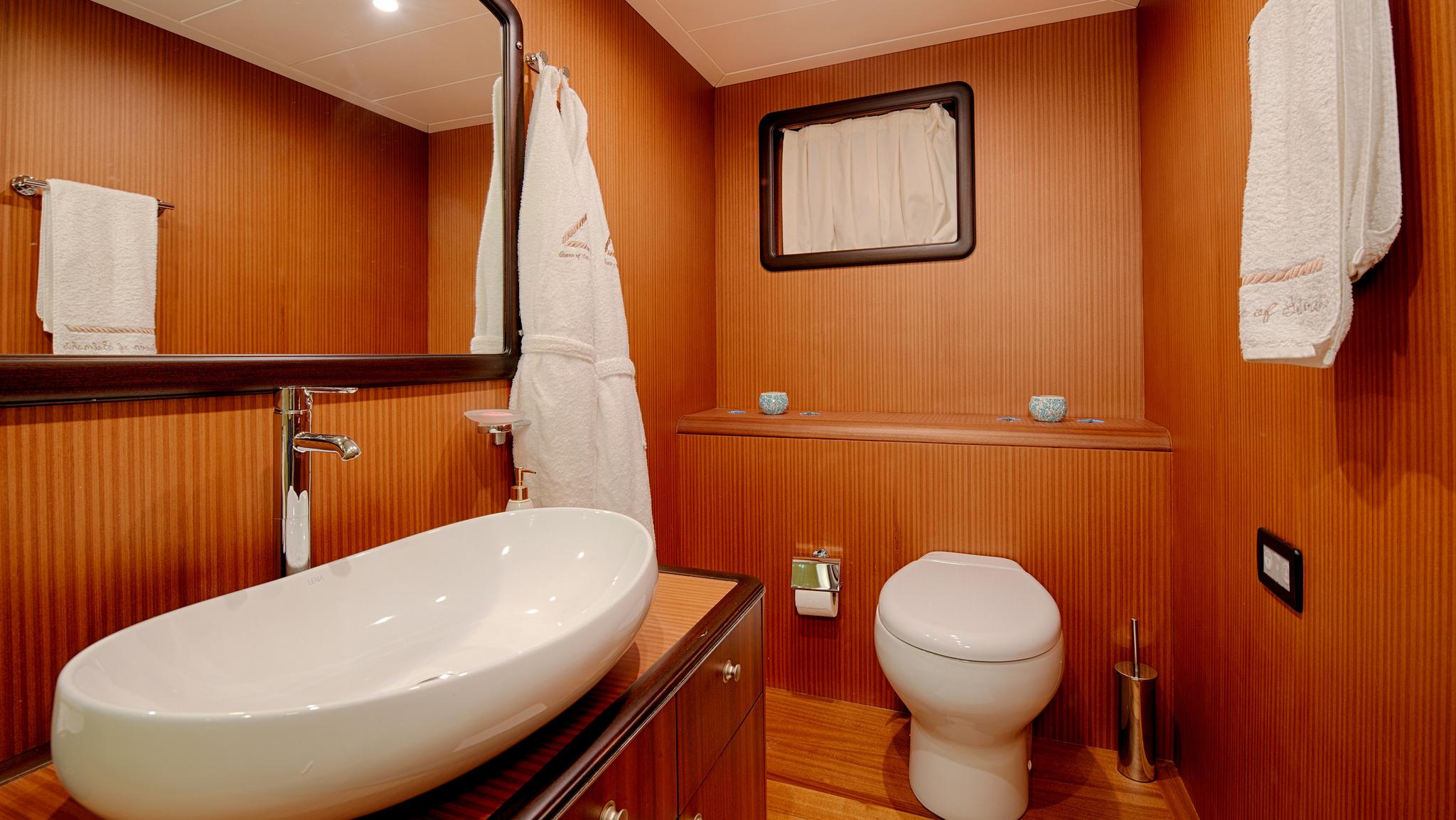 yacht bathroom featuring white oval sink, toilet, and warm wood paneling