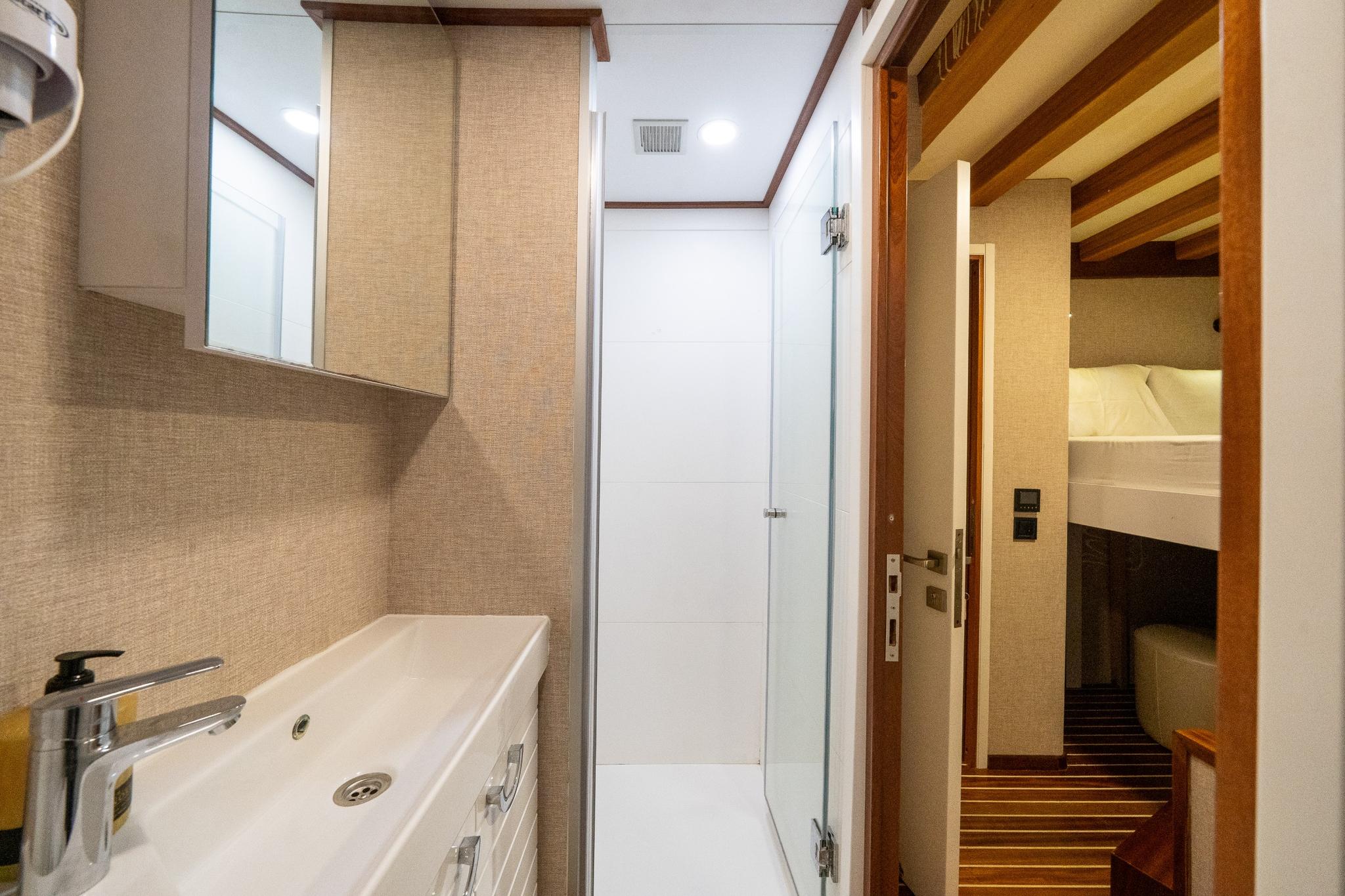 yacht bathroom interior showing white sink, shower stall, beige mosaic tiles and cabin doorway