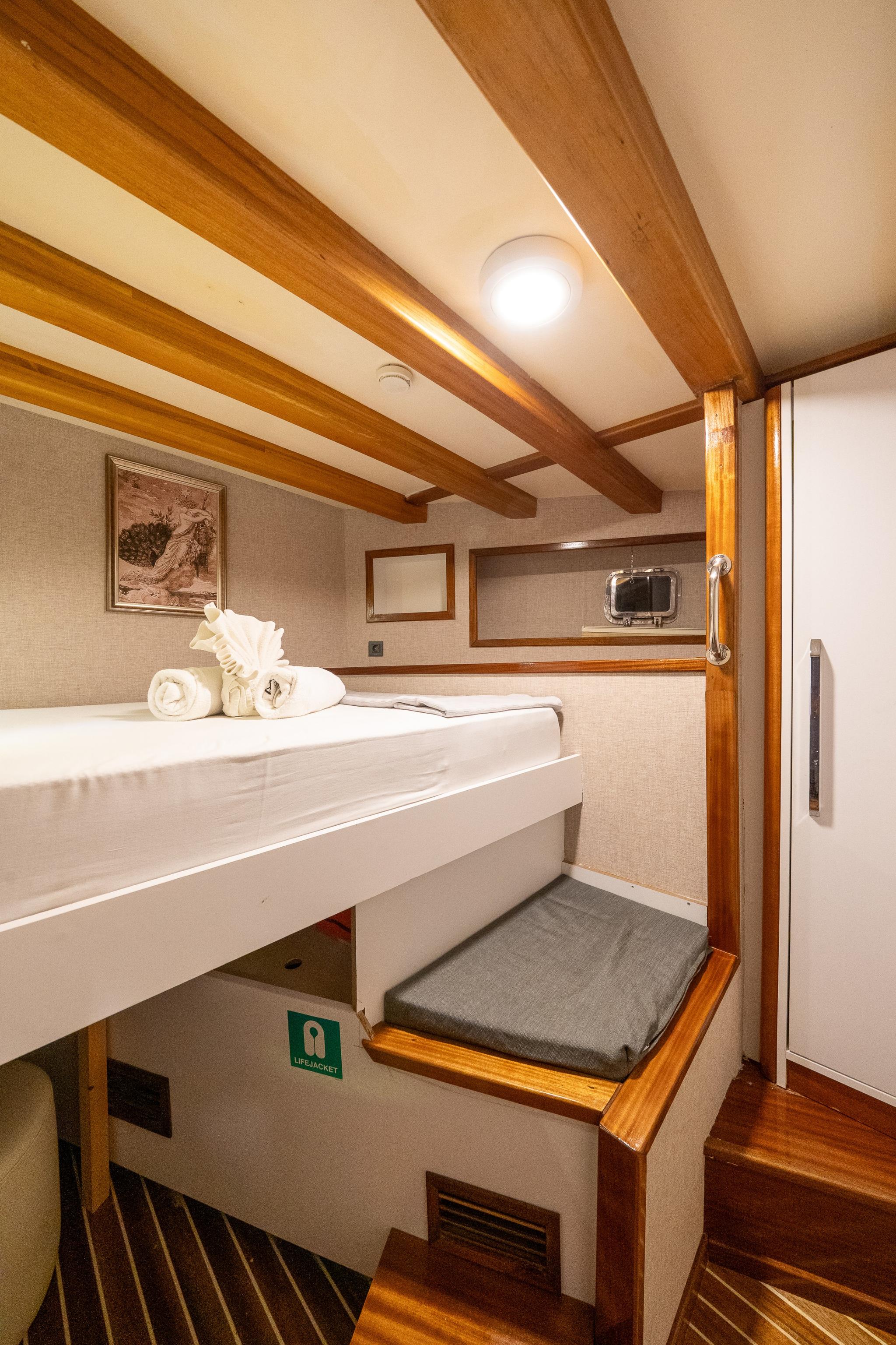yacht guest cabin featuring upper and lower bunk beds with white linens and wooden trim