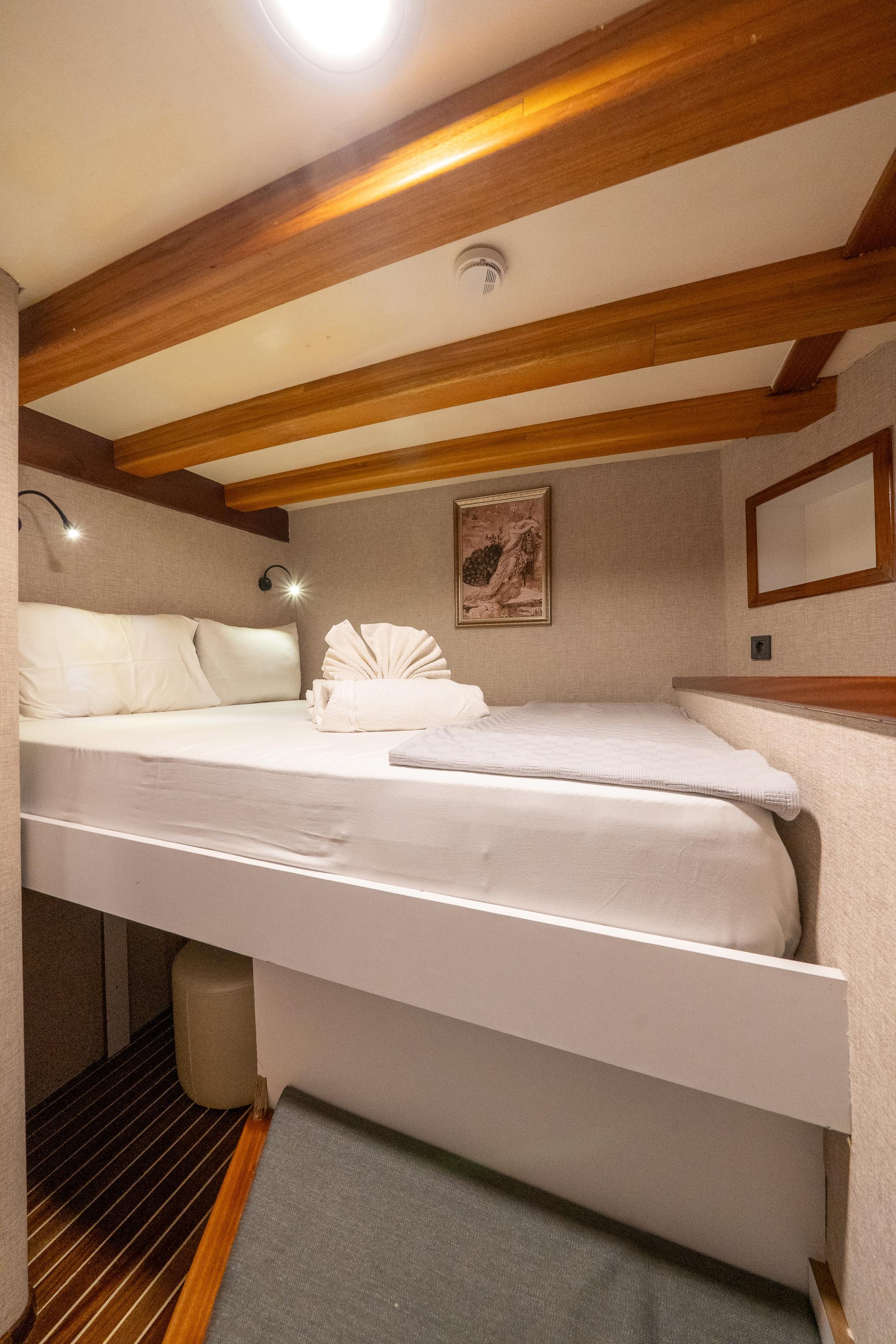 yacht cabin interior featuring double bed with white linens and decorative towel arrangement under wooden ceiling beams