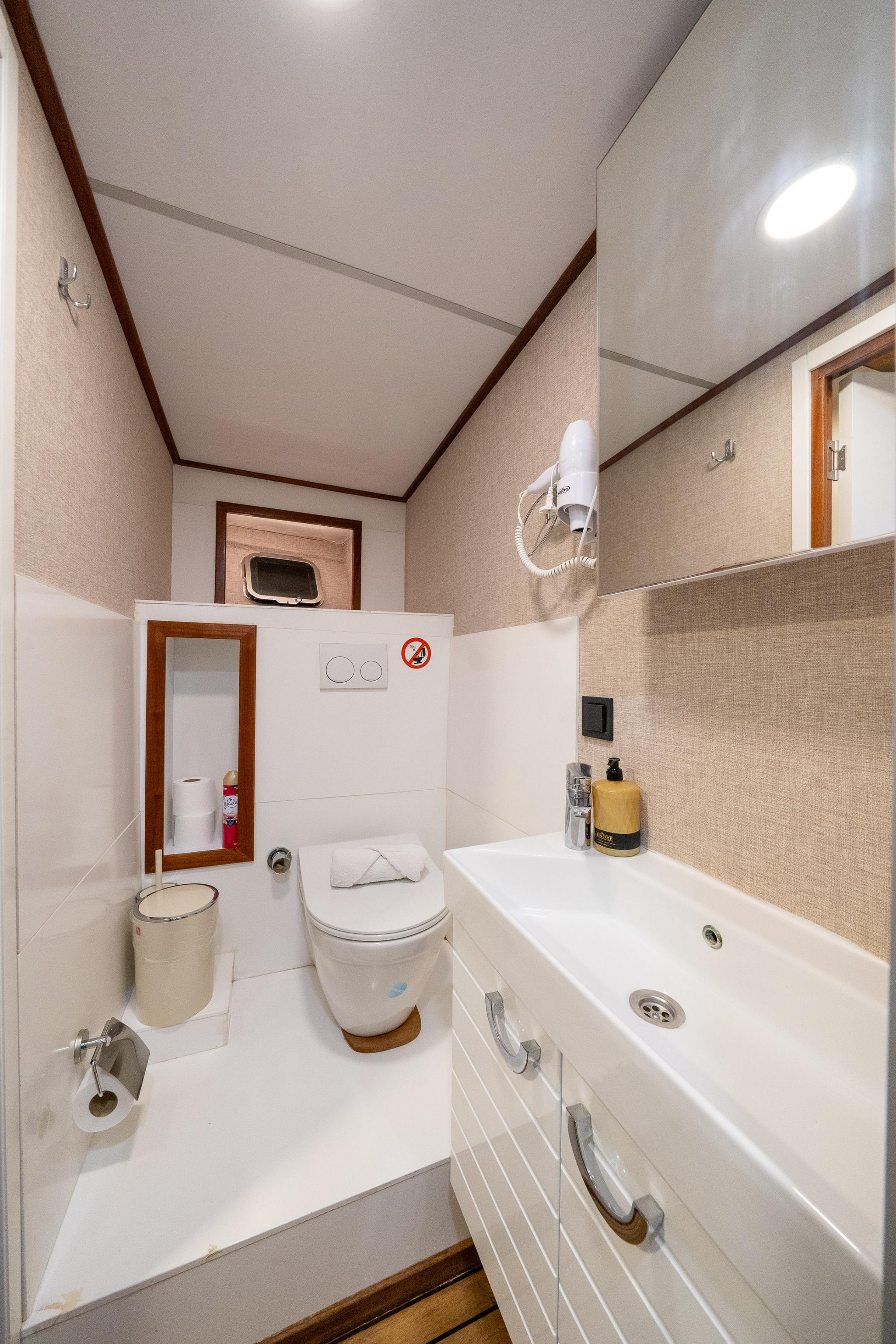 yacht bathroom with white bathtub, toilet, beige textured walls and porthole window