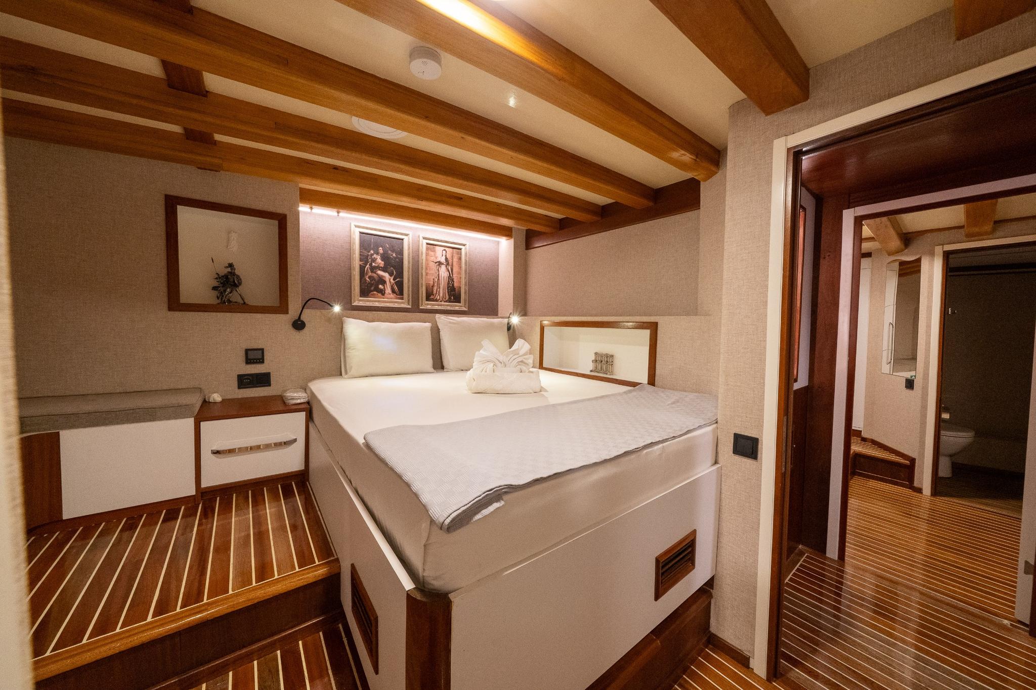 yacht guest cabin featuring double bed, wooden beam ceiling, bedside tables and en-suite bathroom entrance