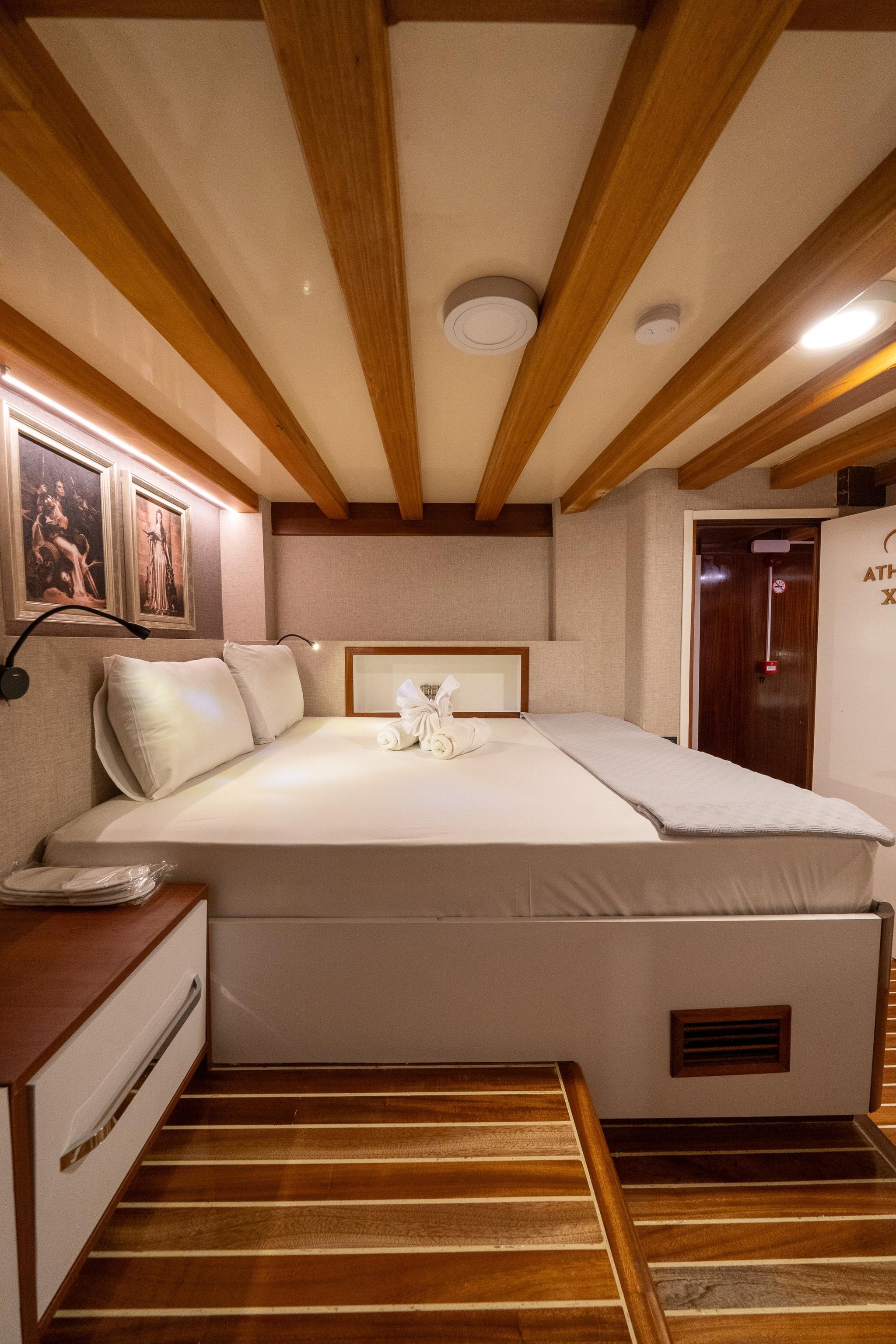 yacht guest cabin featuring double bed with white linens and exposed wooden ceiling beams