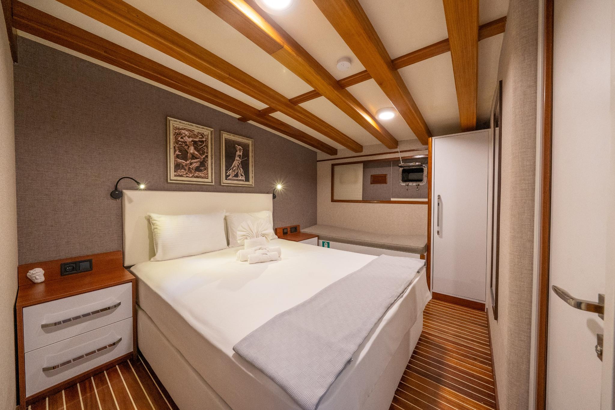 yacht guest cabin featuring double bed, wooden ceiling beams, bedside reading lights and teak flooring