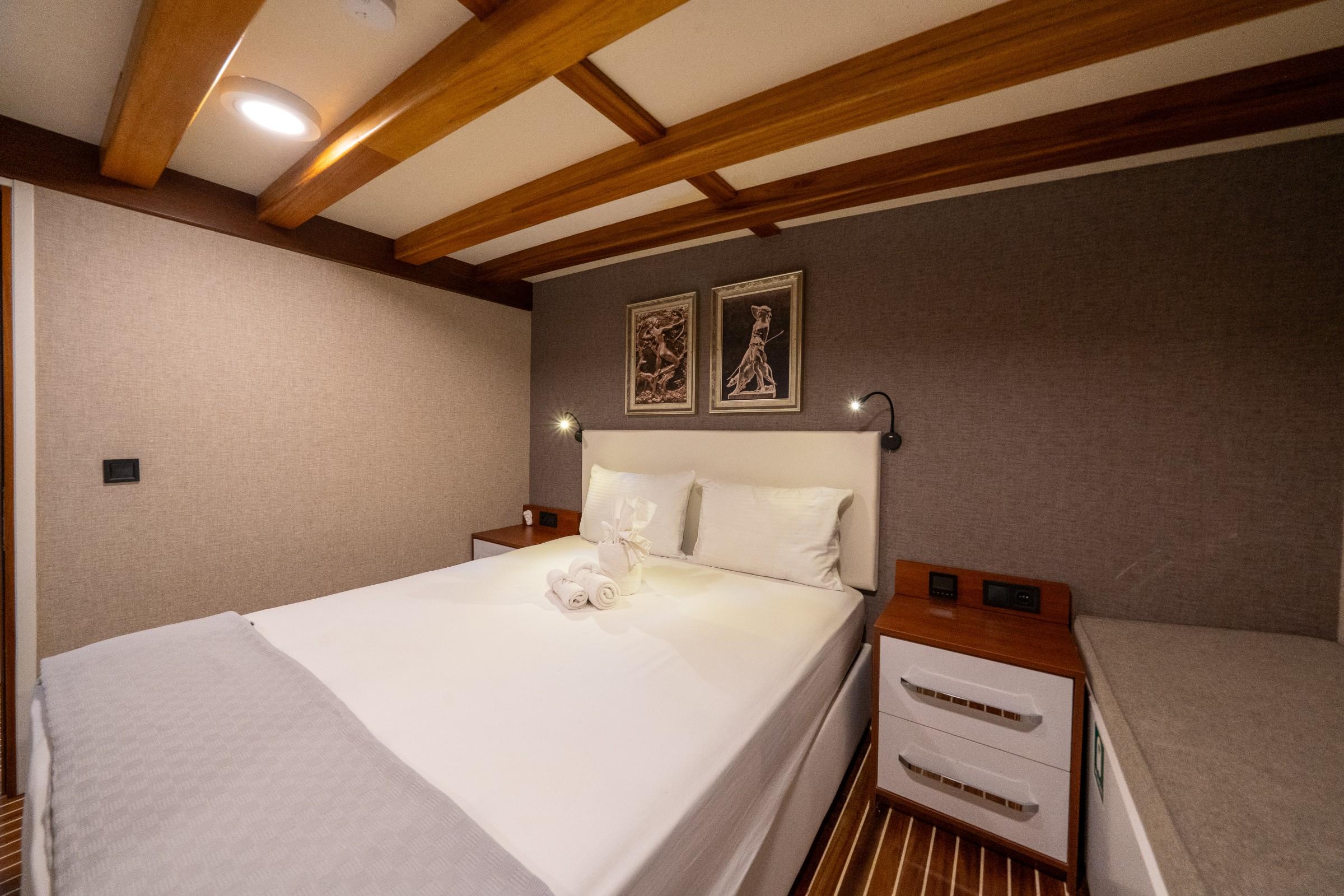 yacht guest cabin featuring double bed with white linens, exposed wooden ceiling beams, and nautical artwork