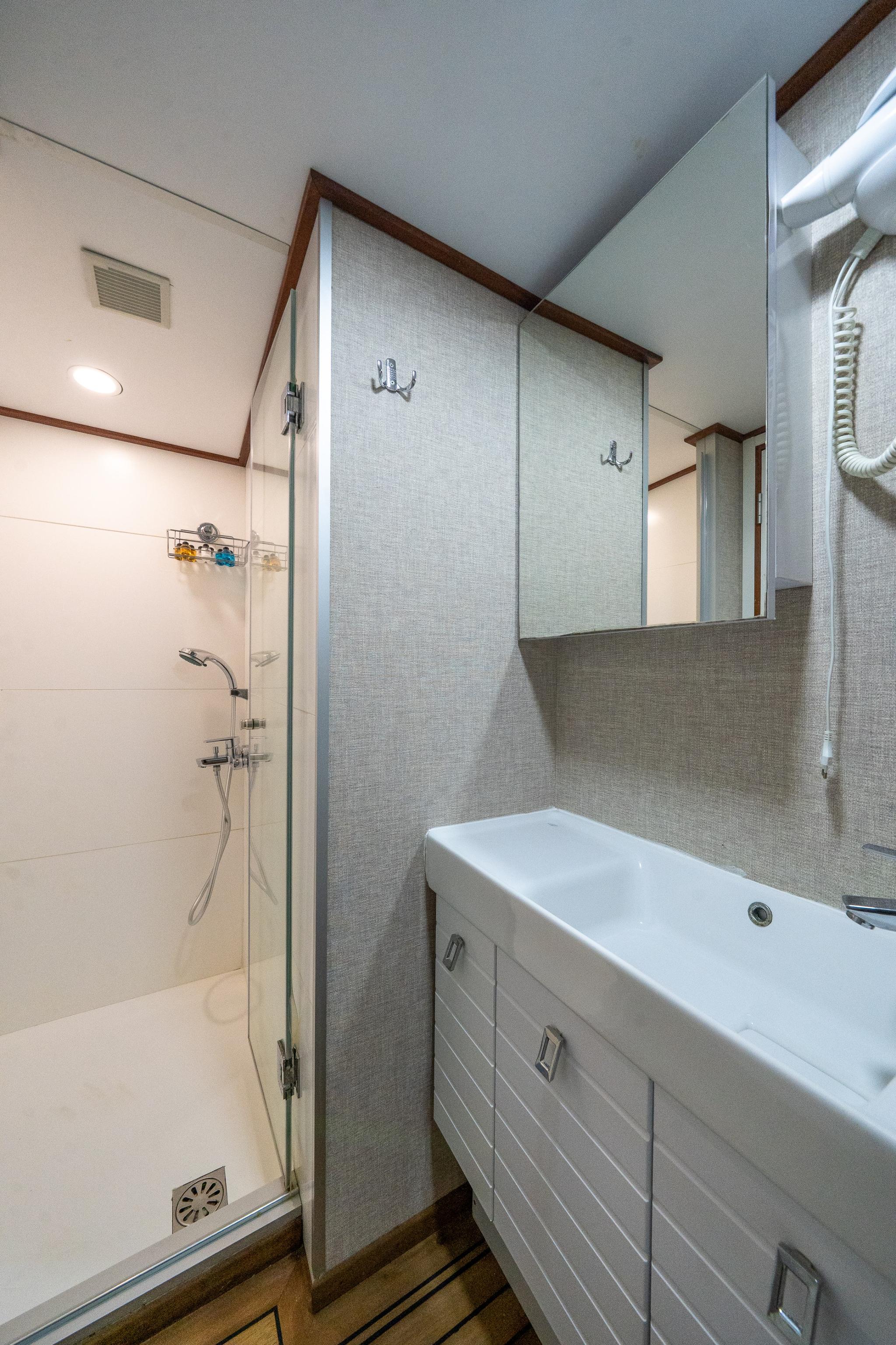 compact yacht bathroom featuring glass shower enclosure, white vanity basin, and gray textured walls