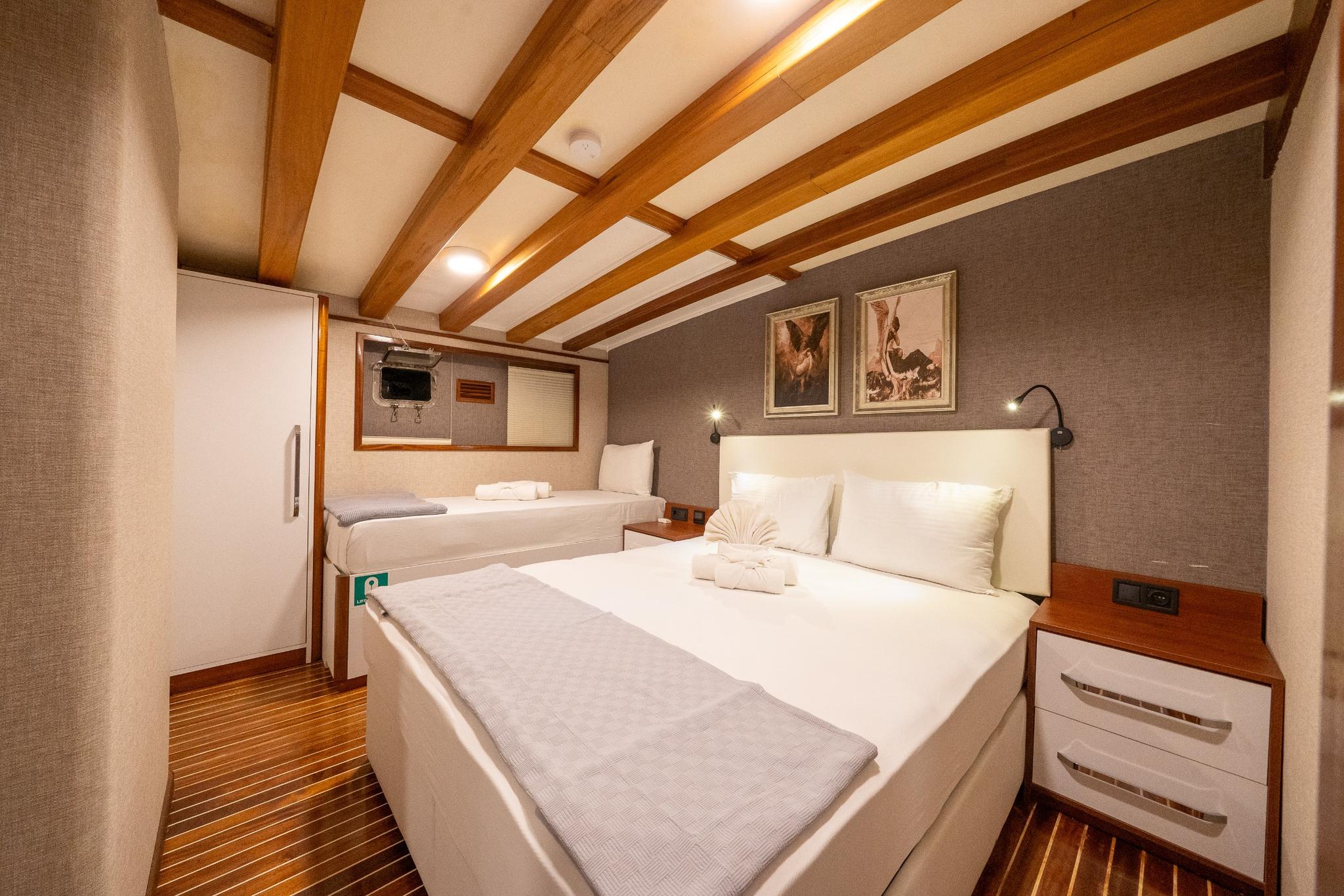 yacht twin cabin with two single beds, exposed wooden ceiling beams, and white upholstered headboards