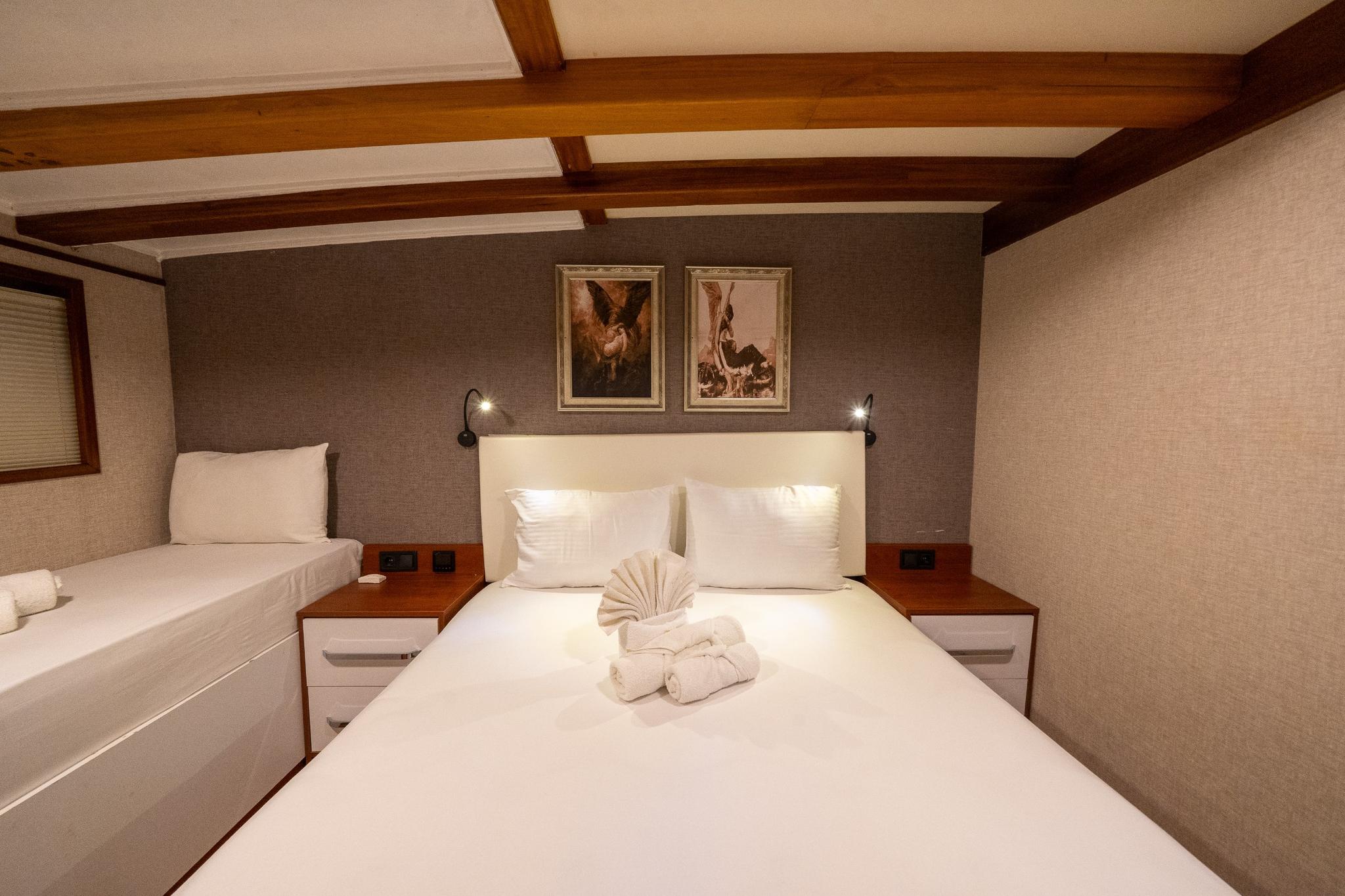 yacht guest cabin featuring double bed with white linens, single berth, exposed ceiling beams and framed artwork