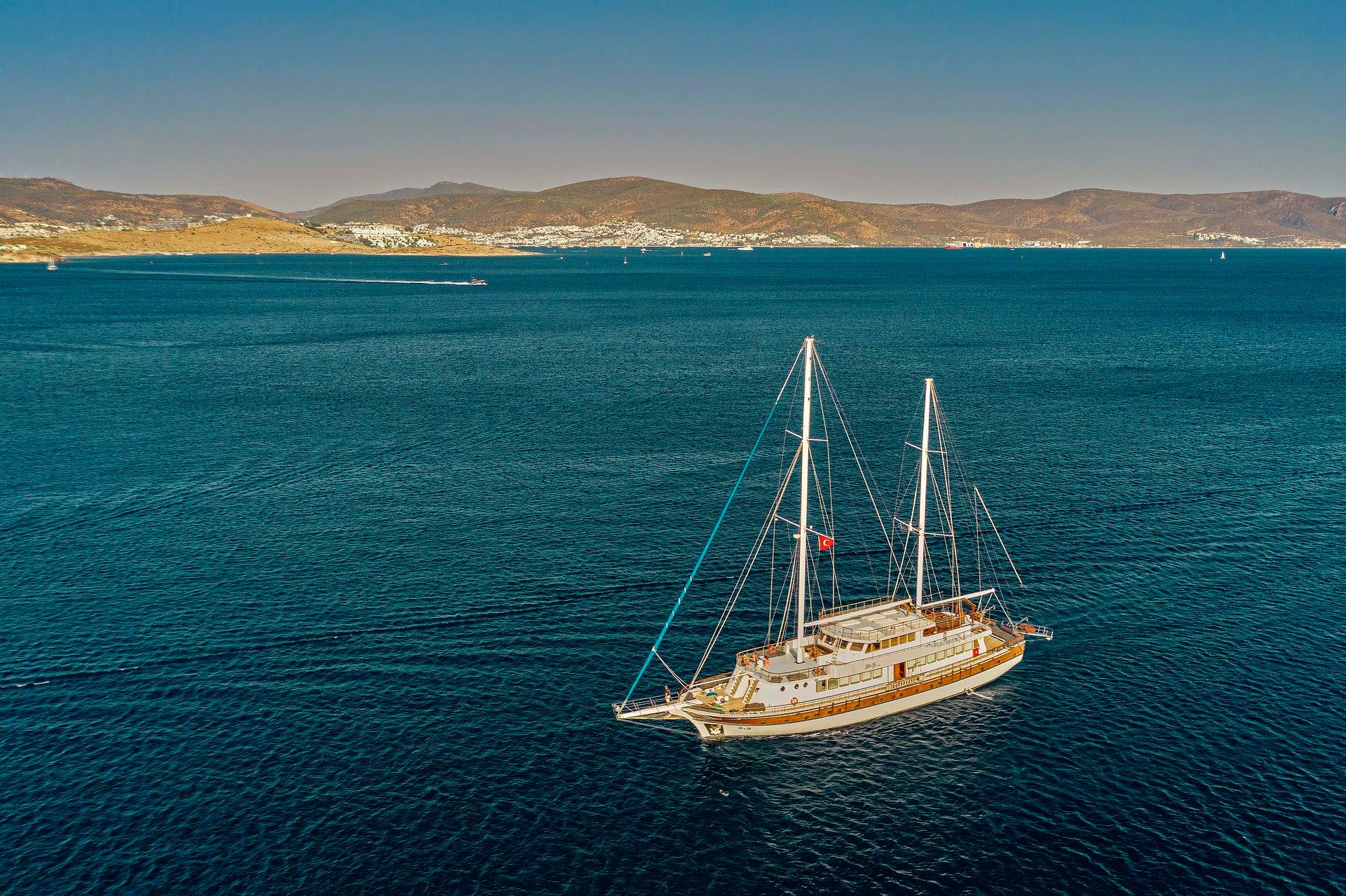 aerial view of traditional wooden gulet yacht anchored in turquoise bay with mountainous coastline