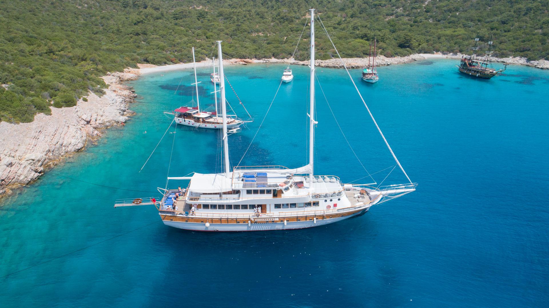 aerial view of white traditional gulet yacht anchored in crystal clear turquoise bay with rocky coastline