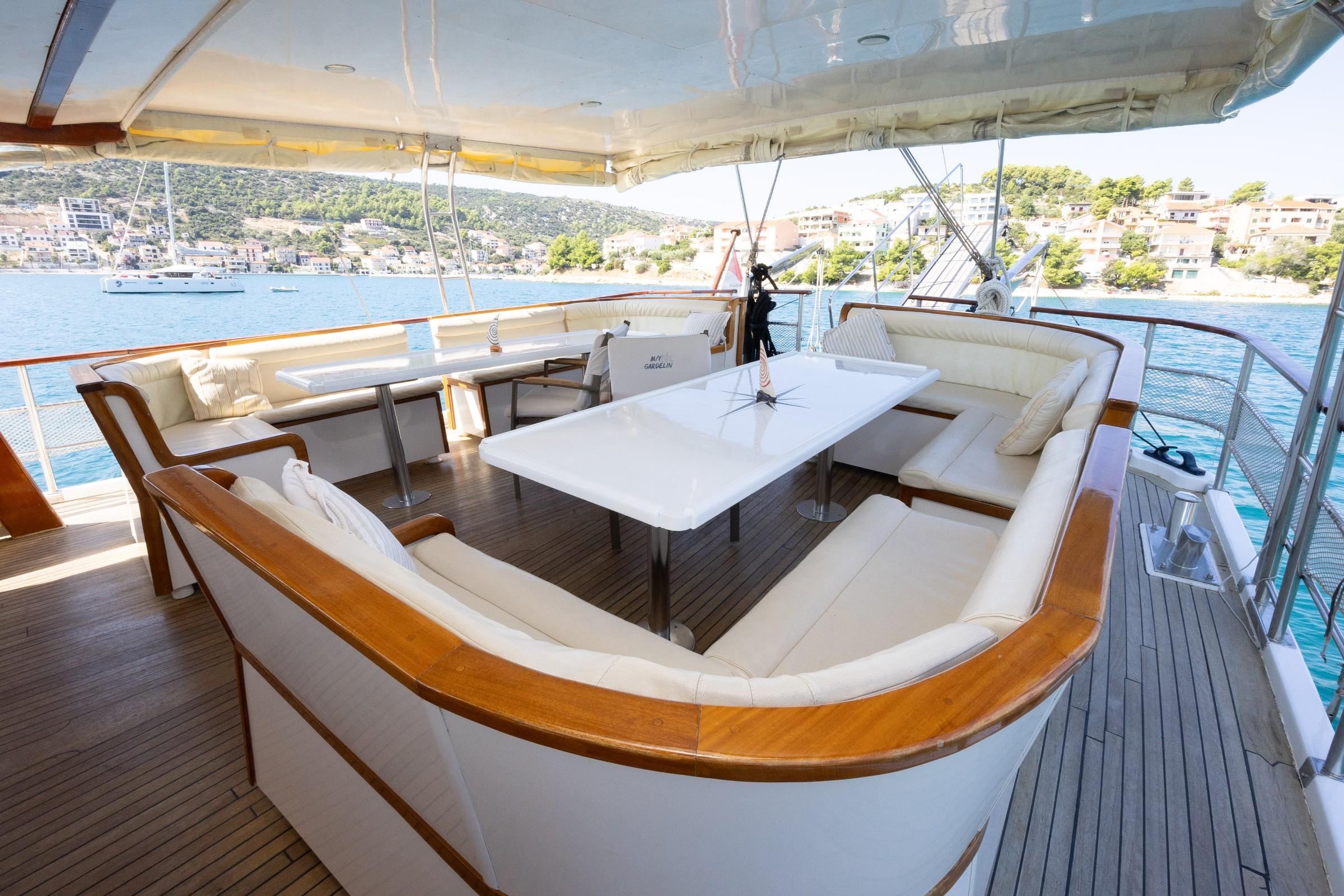 gulet aft deck with cream U-shaped seating, white dining table, teak decking, and coastal town backdrop