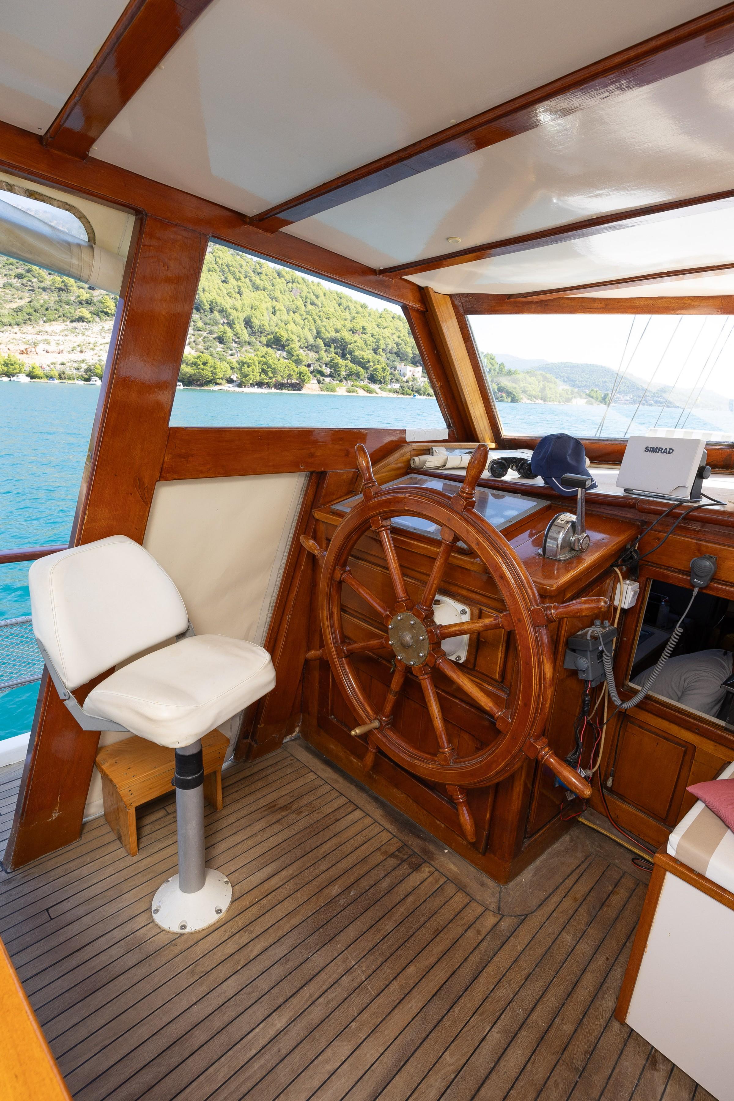 Traditional wooden helm station with large ship's wheel, Simrad chartplotter, and captain's seat inside gulet wheelhouse