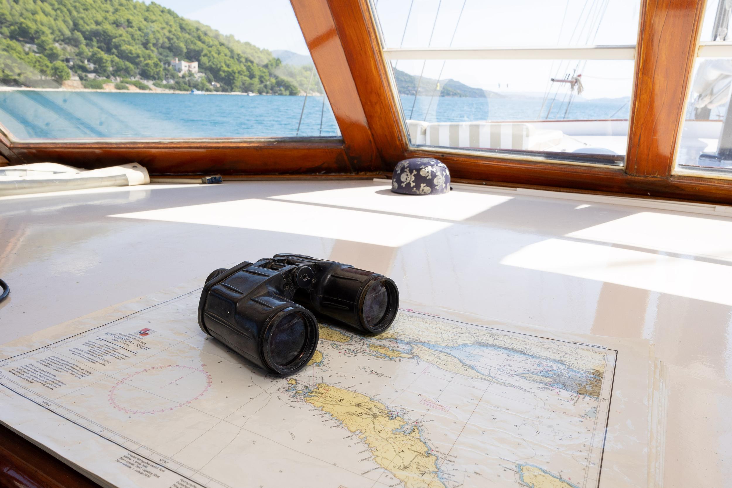 gulet helm station with nautical chart, black binoculars and wooden framed windows overlooking sea
