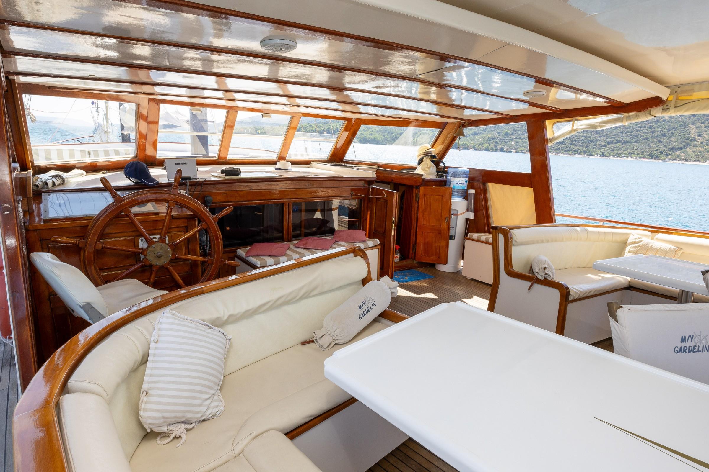 Gulet MV Gardelin open cockpit with wooden helm wheel, Simrad instruments, cream cushioned sofas and dining table