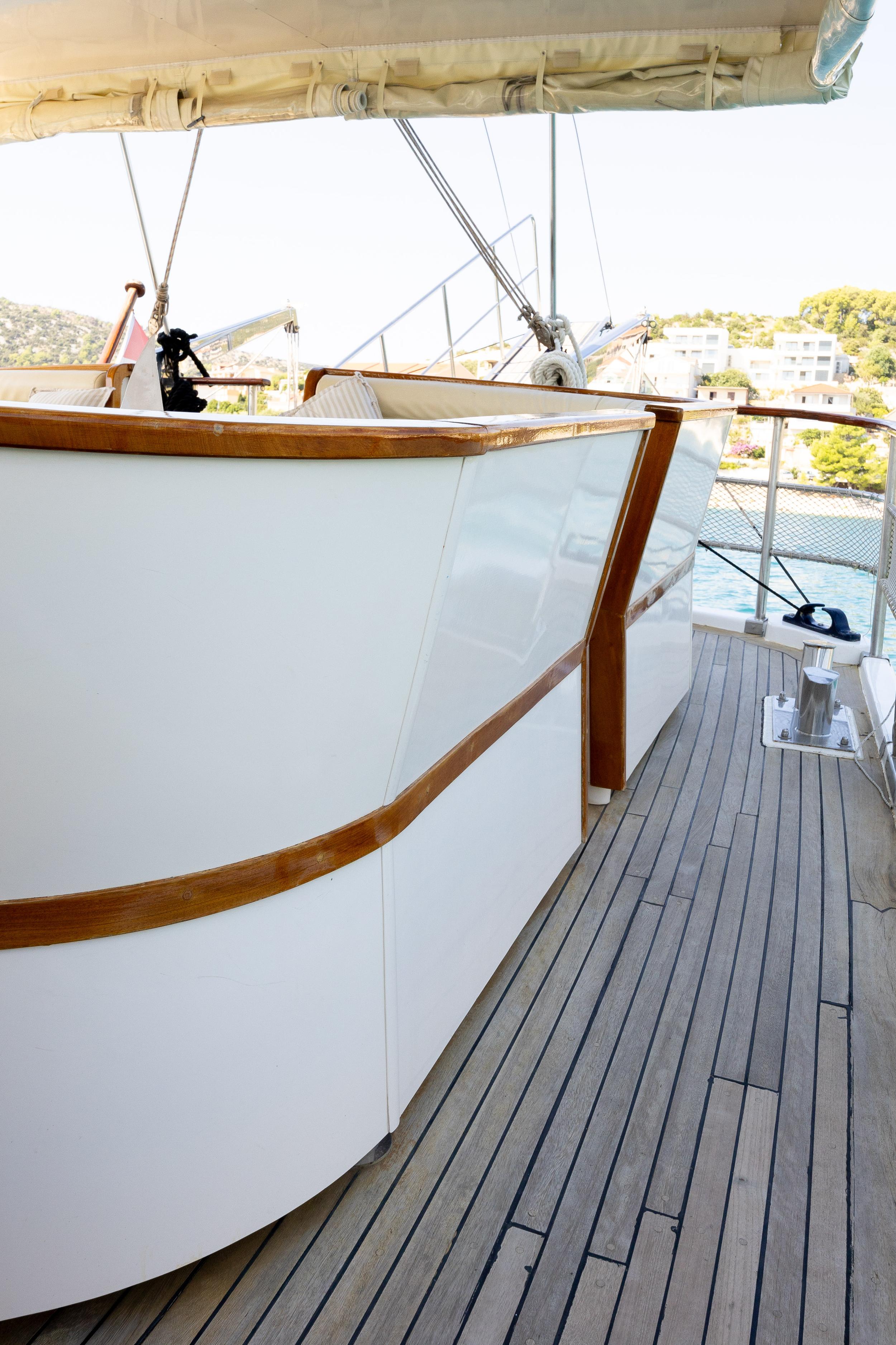 Gulet starboard side deck with grey teak planking, white hull and varnished timber trim, moored in harbour