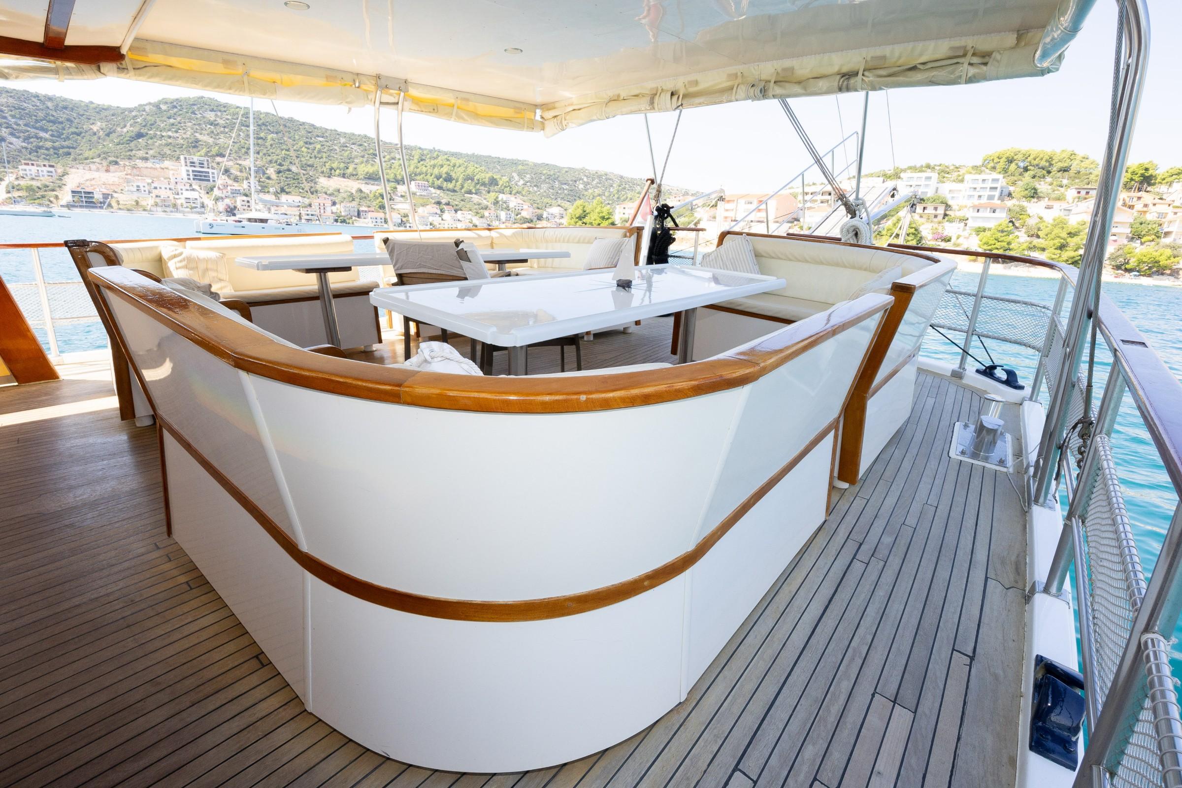 Gulet aft deck with curved white and teak seating, rectangular dining table, and cream canopy overhead