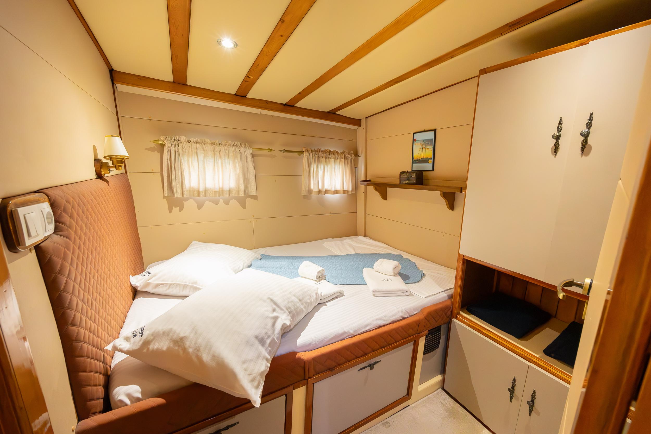 Gulet double cabin with quilted headboard, white bedding, folded towels and built-in wardrobe