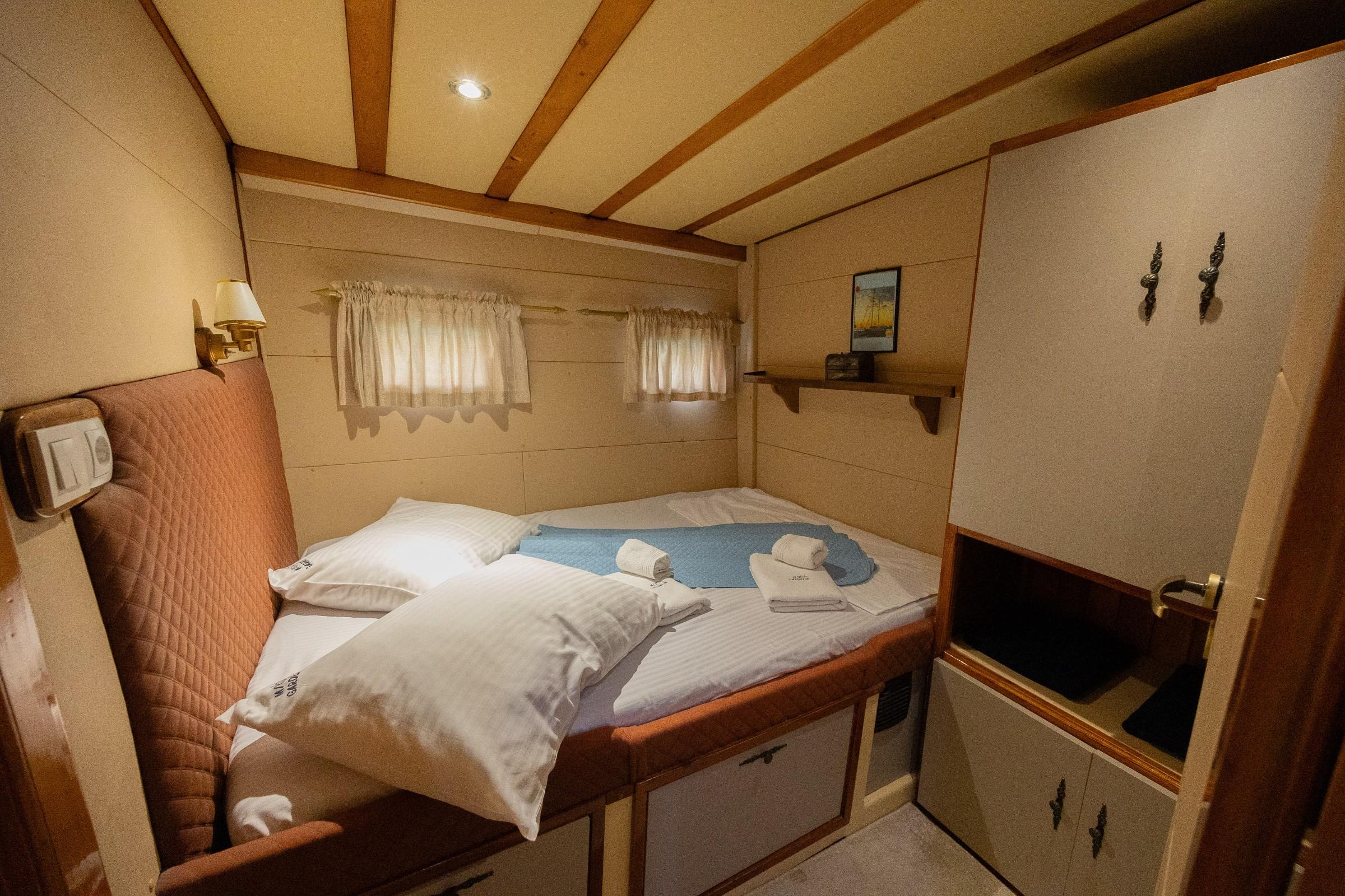 Gulet double cabin with quilted pink headboard, white bedding, folded towels, and built-in wardrobe